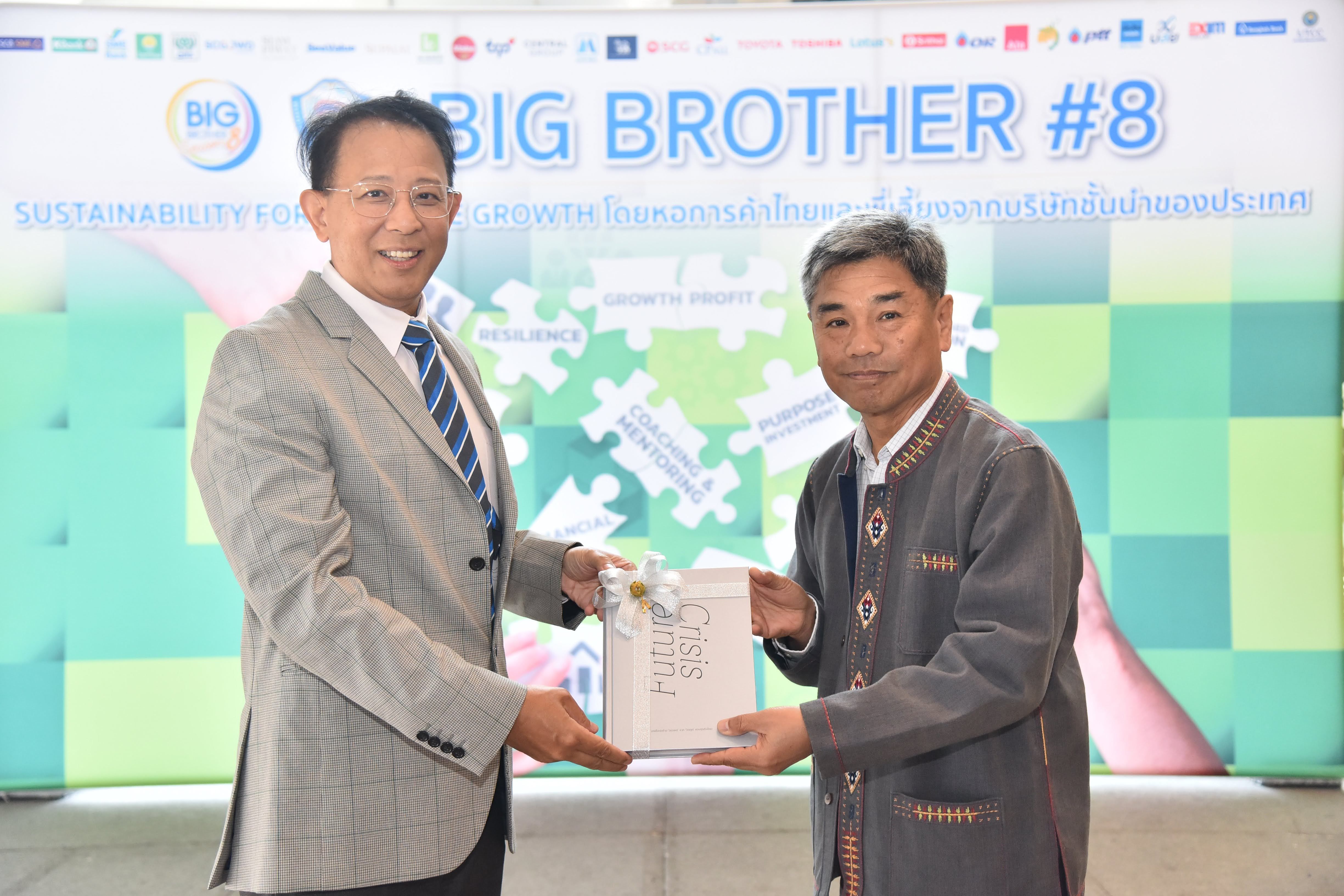Two men on stage exchange a document in front of a screen displaying 'BIG BROTHER #8'.