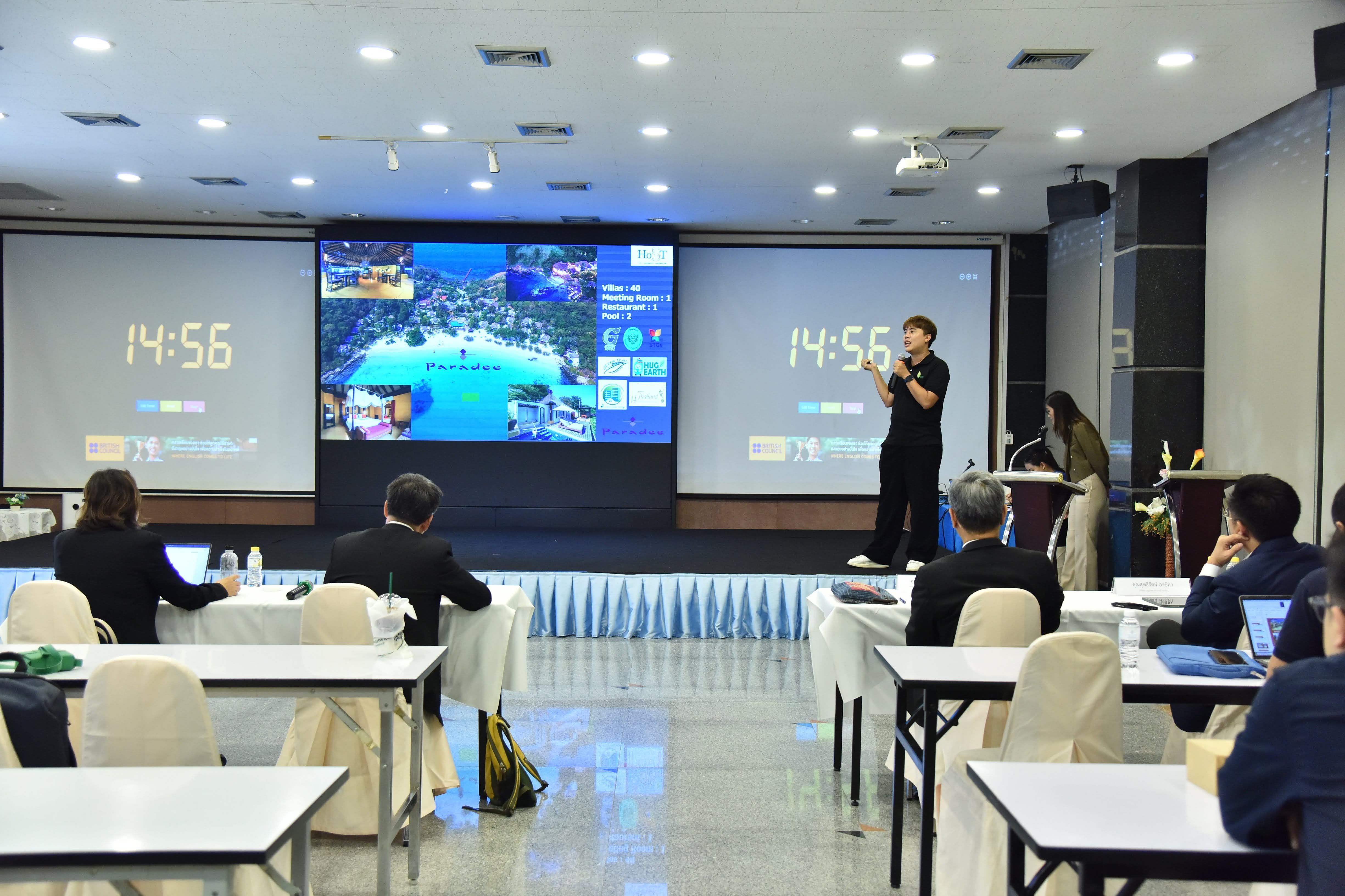 Presenter on stage with two large screens showing a timer and content to an audience.