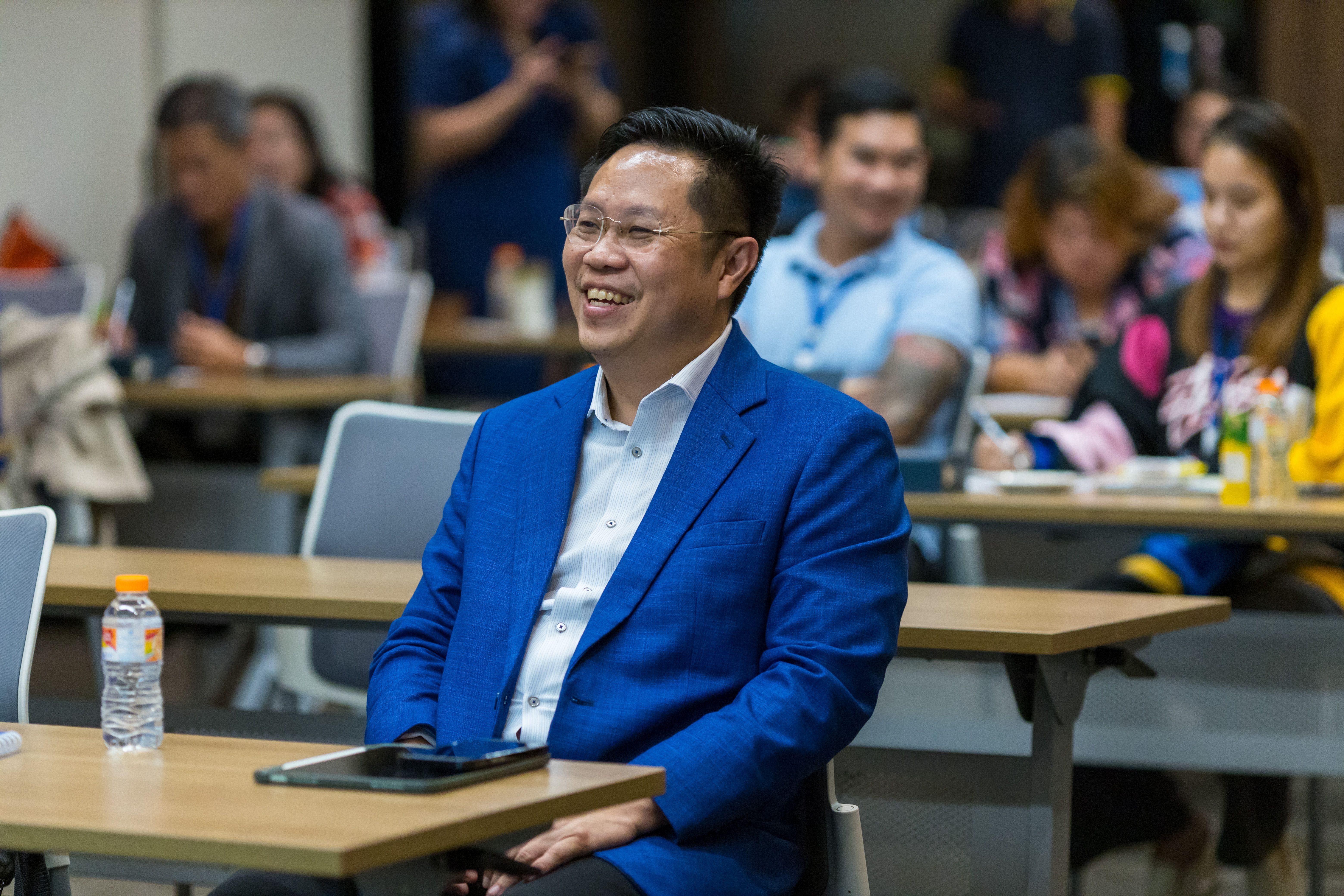 Man in a vibrant blue suit smiles, engaged during a conference session.