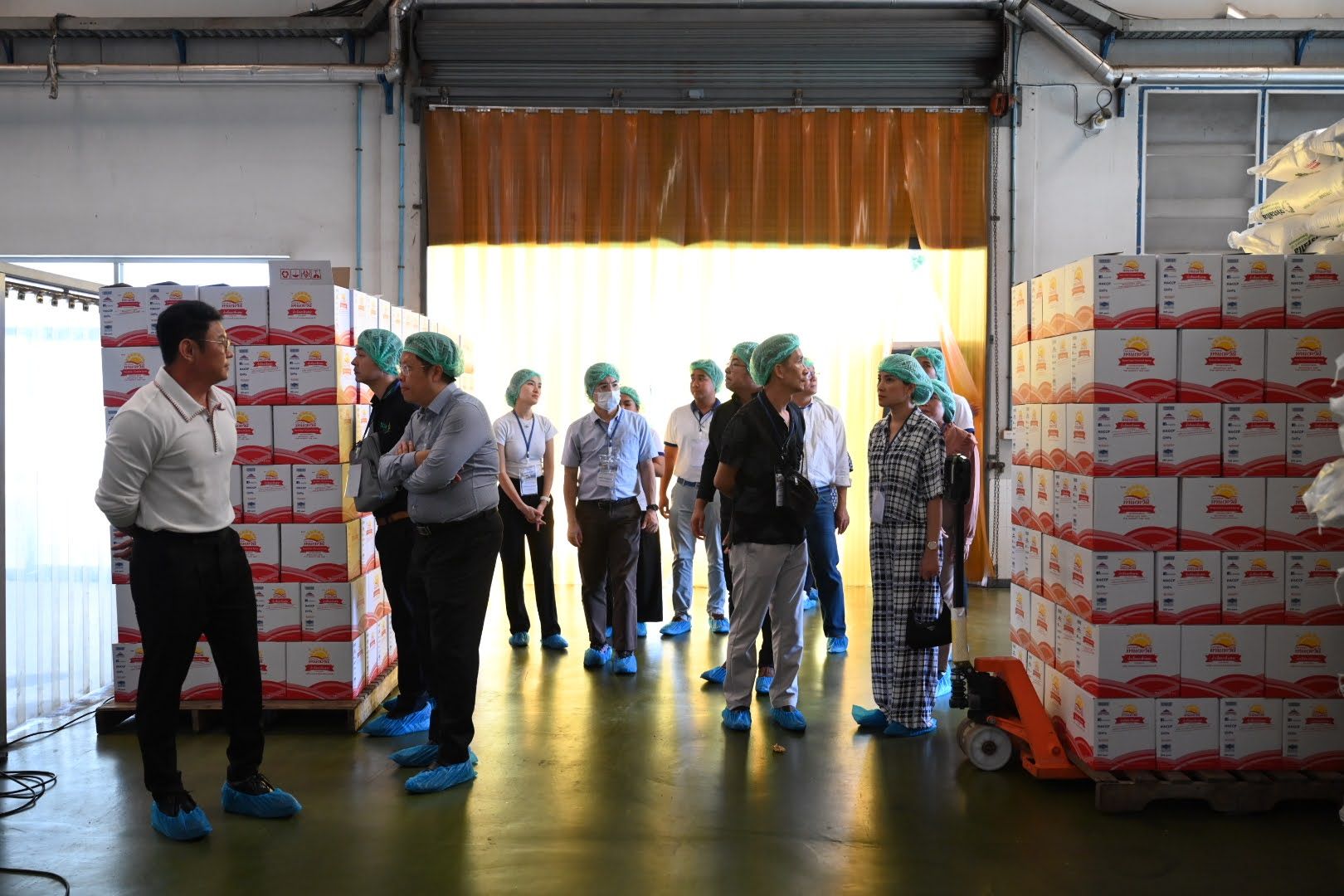 Group of people wearing protective gear inspecting a clean industrial warehouse with stacked boxes.