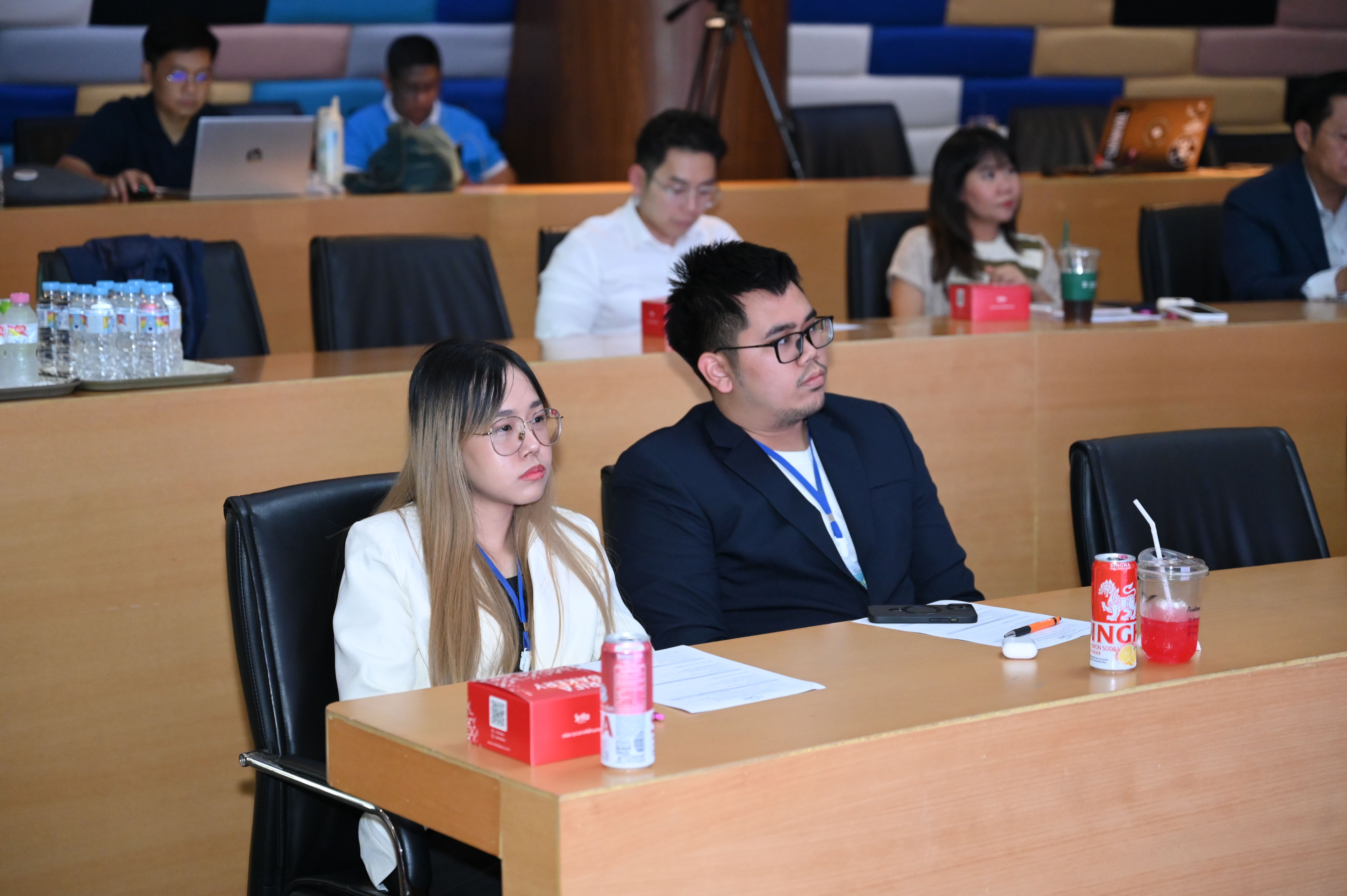 Two attentive attendees, a woman and a man, watch a presentation in a conference room.