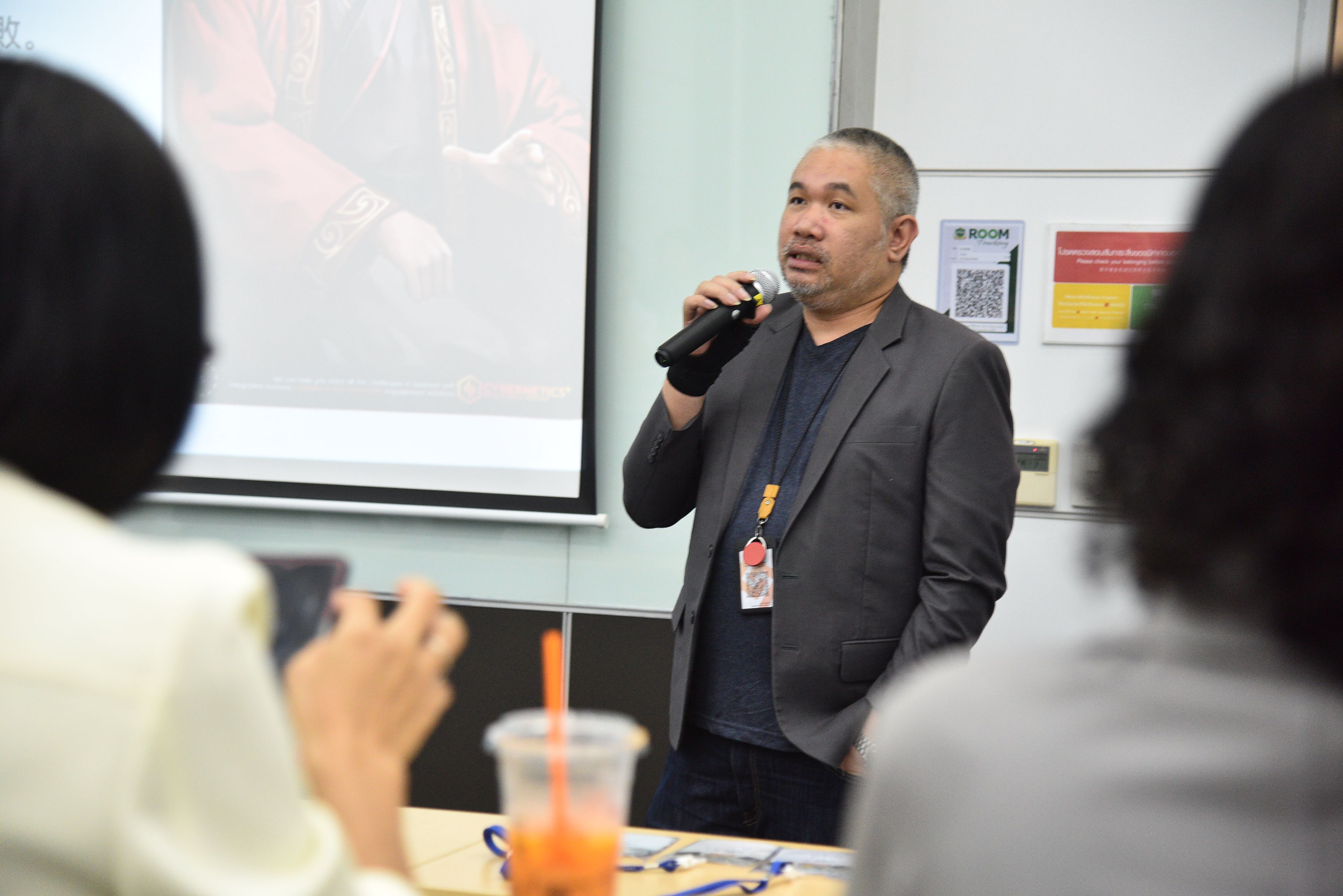 Man with microphone presents to an audience in a conference room.