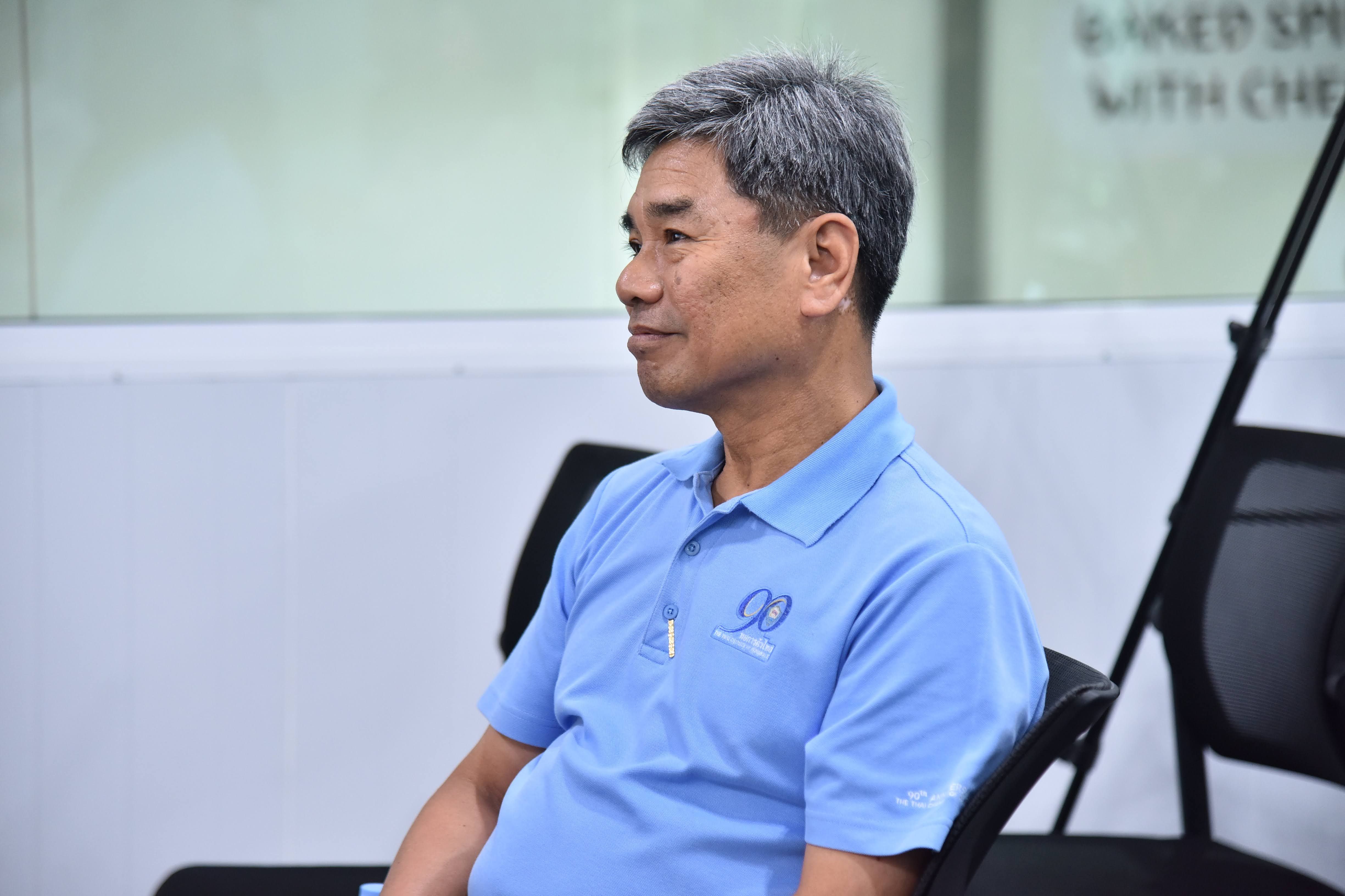 Asian man with gray hair in a blue polo shirt, sitting and looking right.
