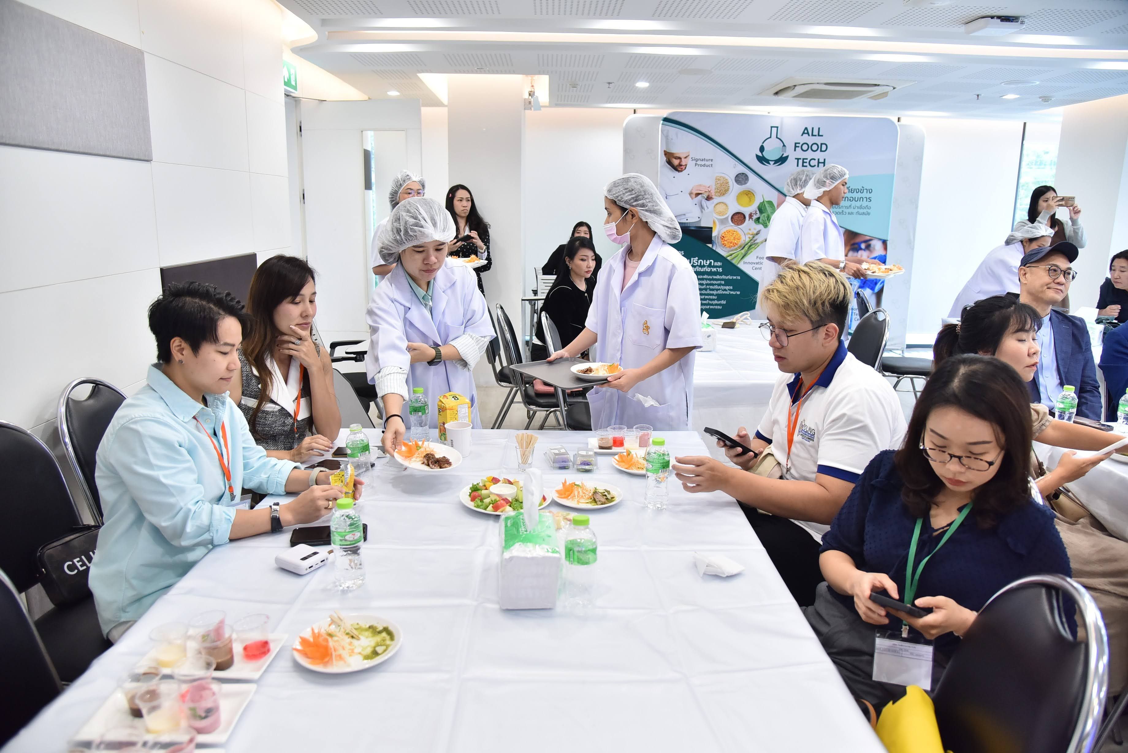 Staff in white uniforms serve small salads to attendees seated at a conference table.