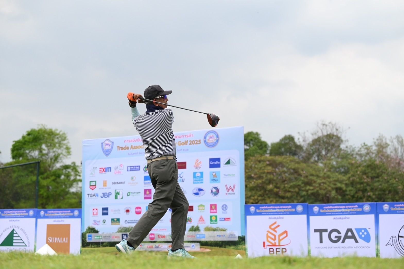 A male golfer in a striped shirt powerfully swings his driver on a green golf course.