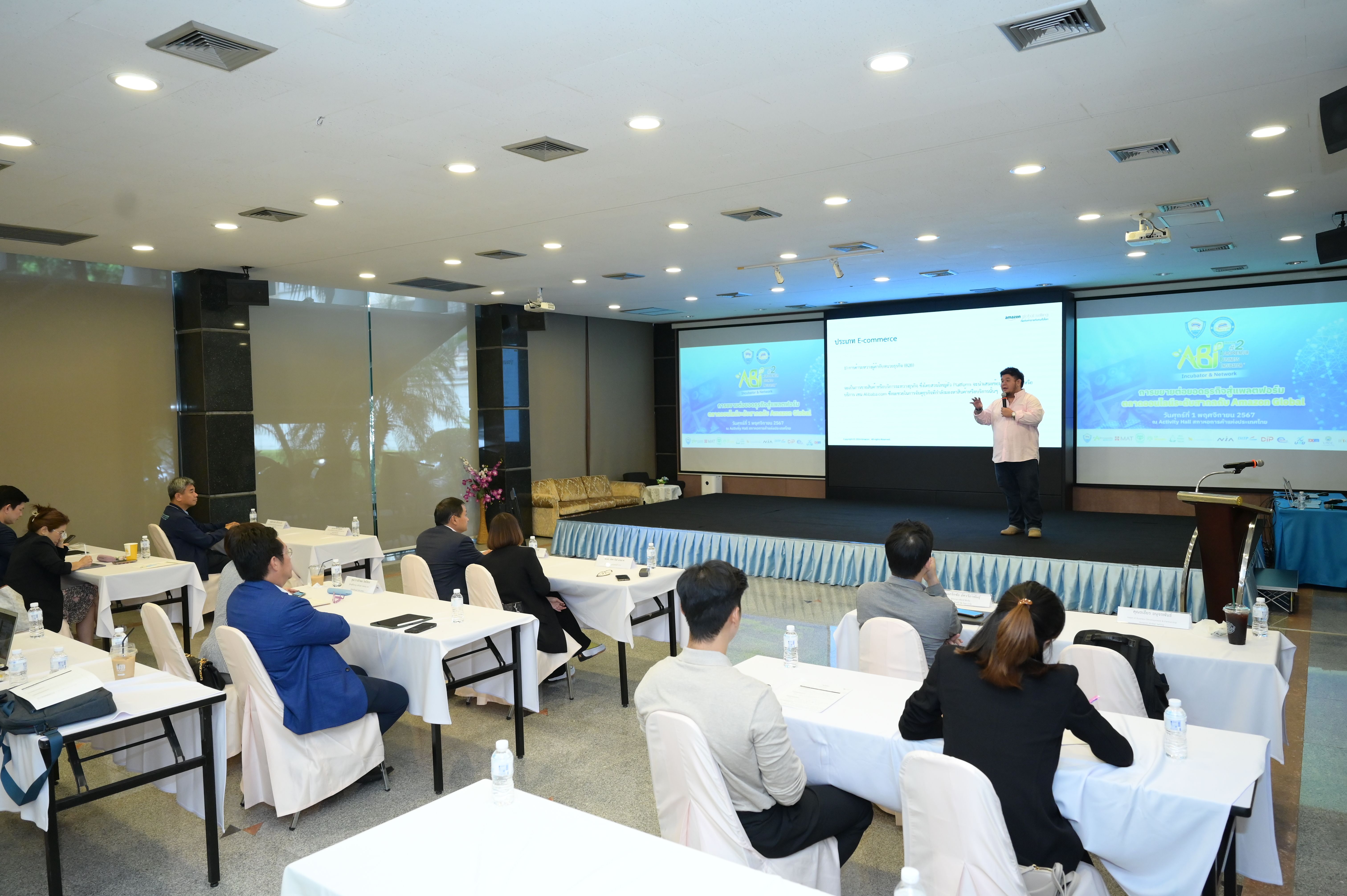 Speaker on stage addressing an audience in a well-lit conference room.