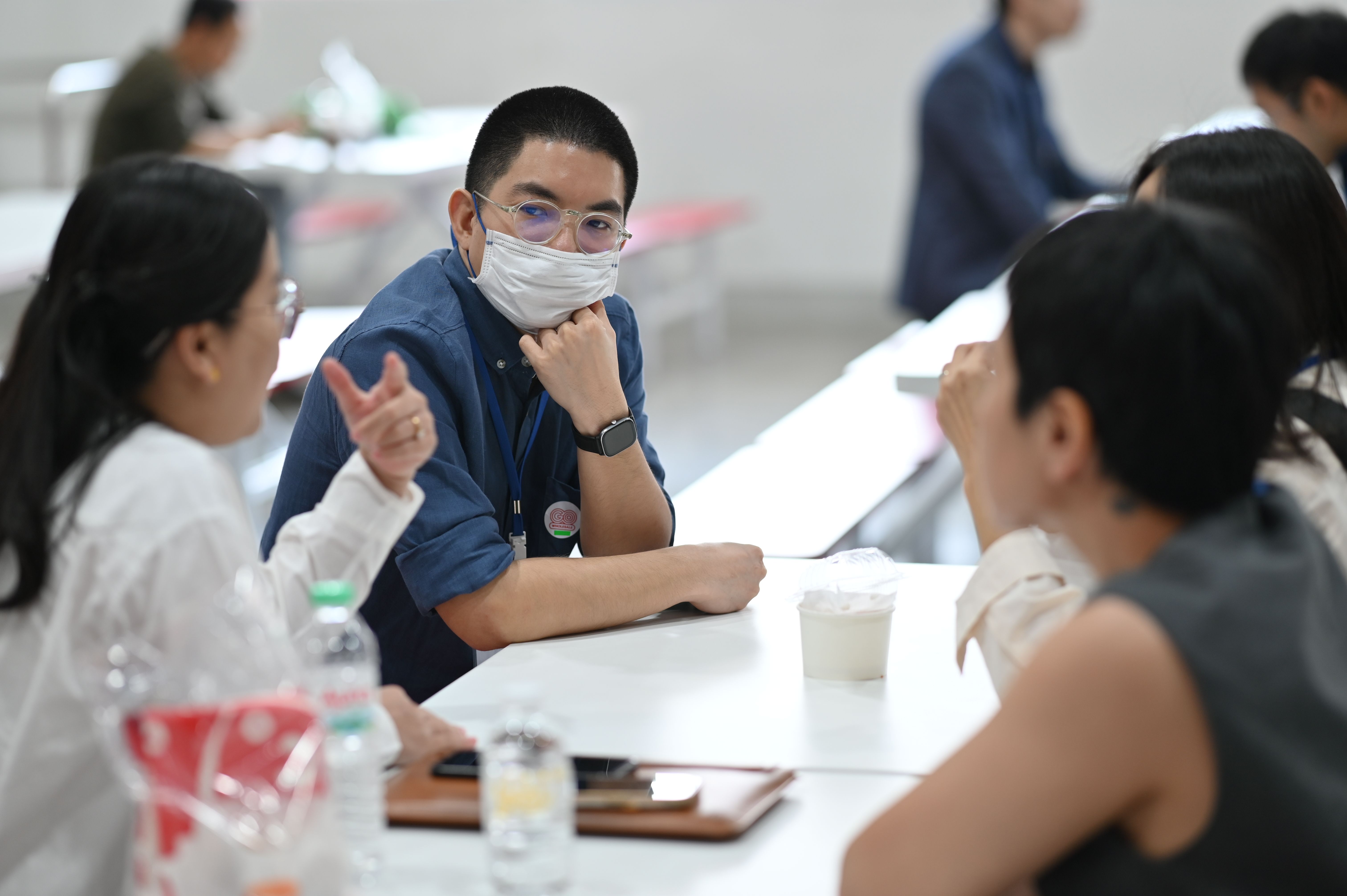 Man in glasses and face mask sitting at a table, looking engaged in conversation.