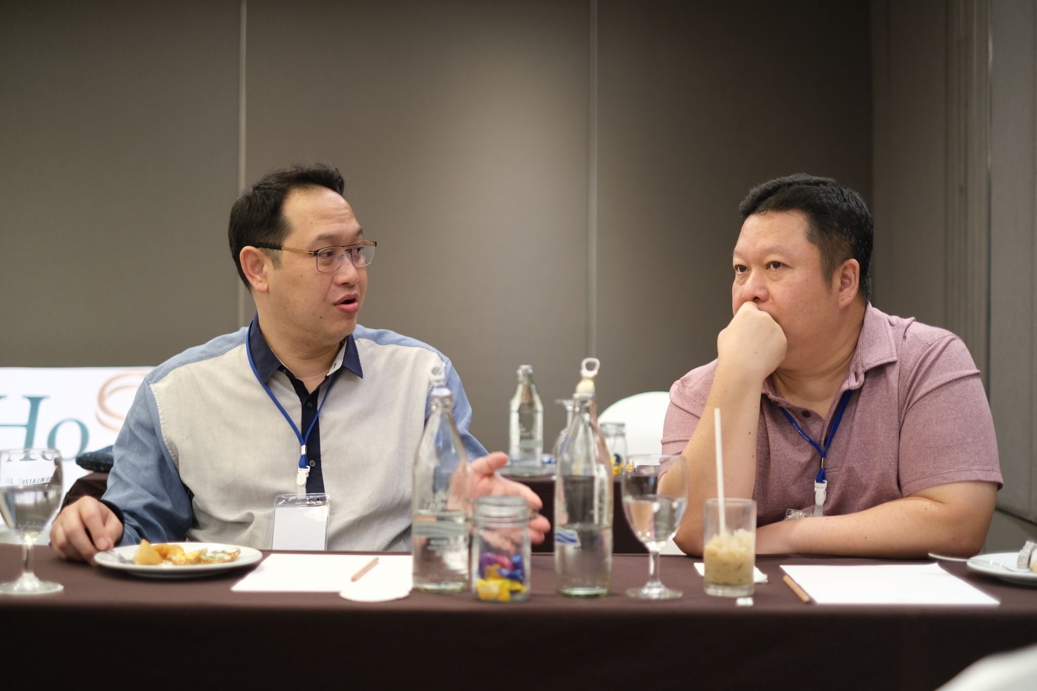 Two men discussing at a conference table, one gesturing while speaking, the other listening intently.