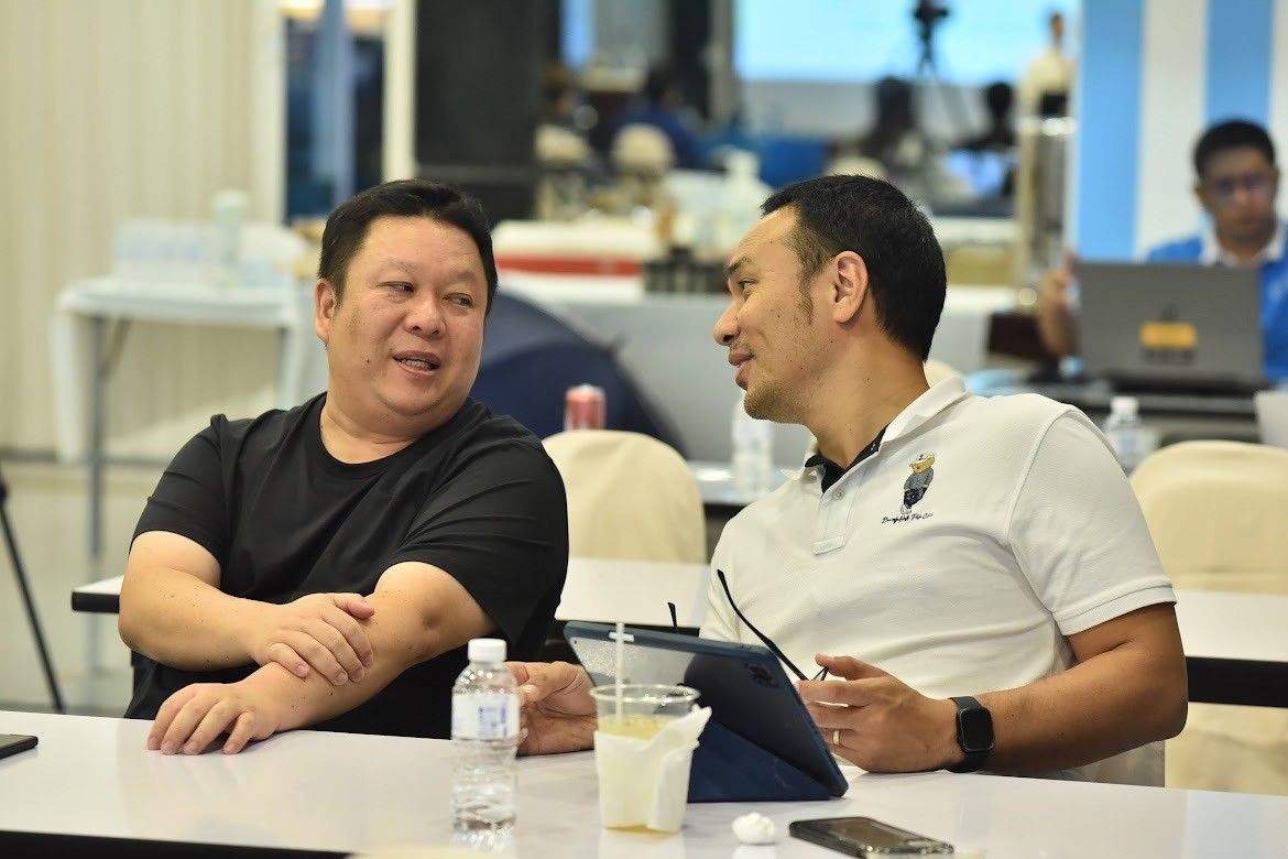 Two men in a meeting room engaging in a focused conversation at a table.