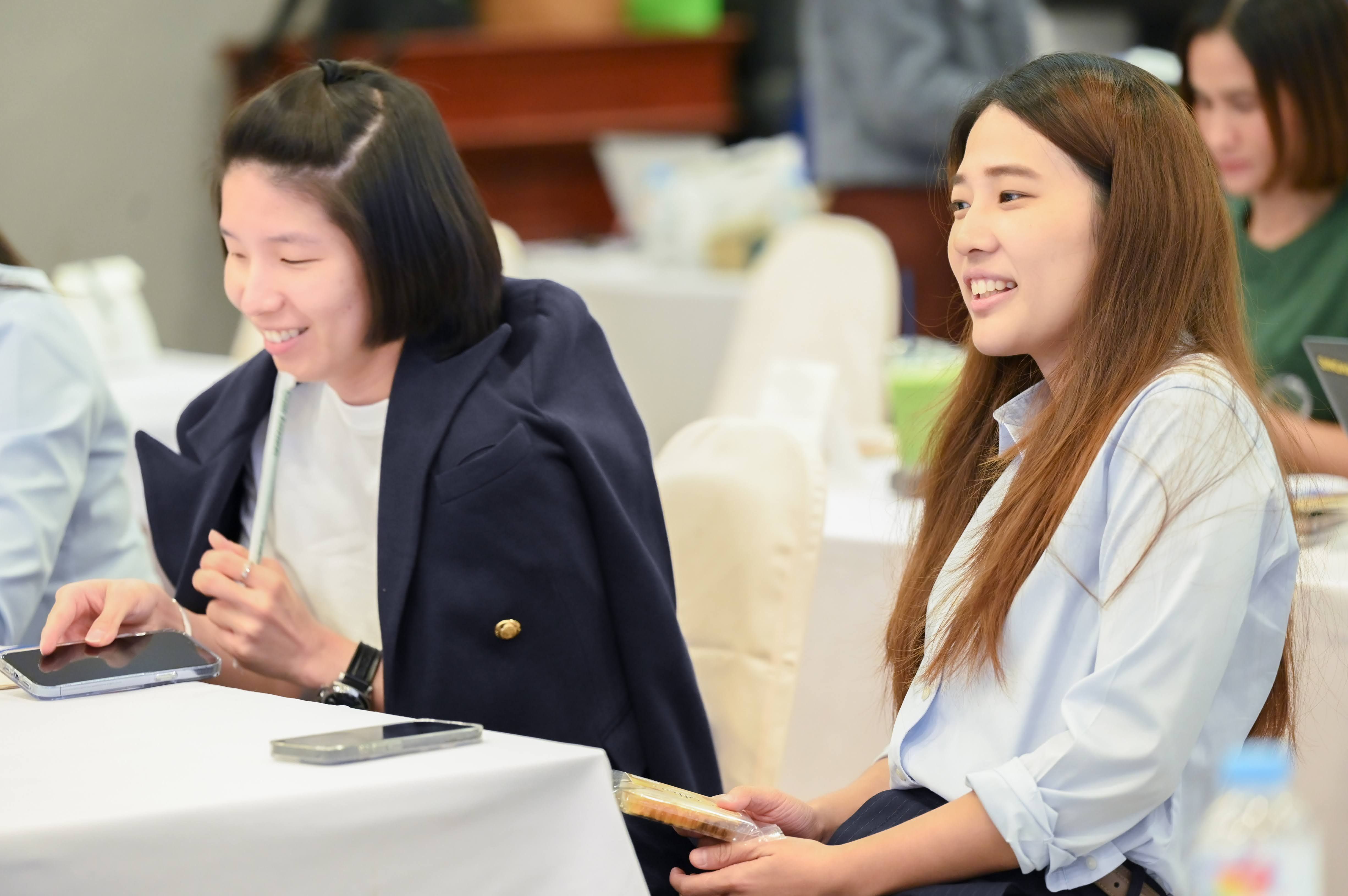 Two young Asian women smiling and engaged during a professional meeting.