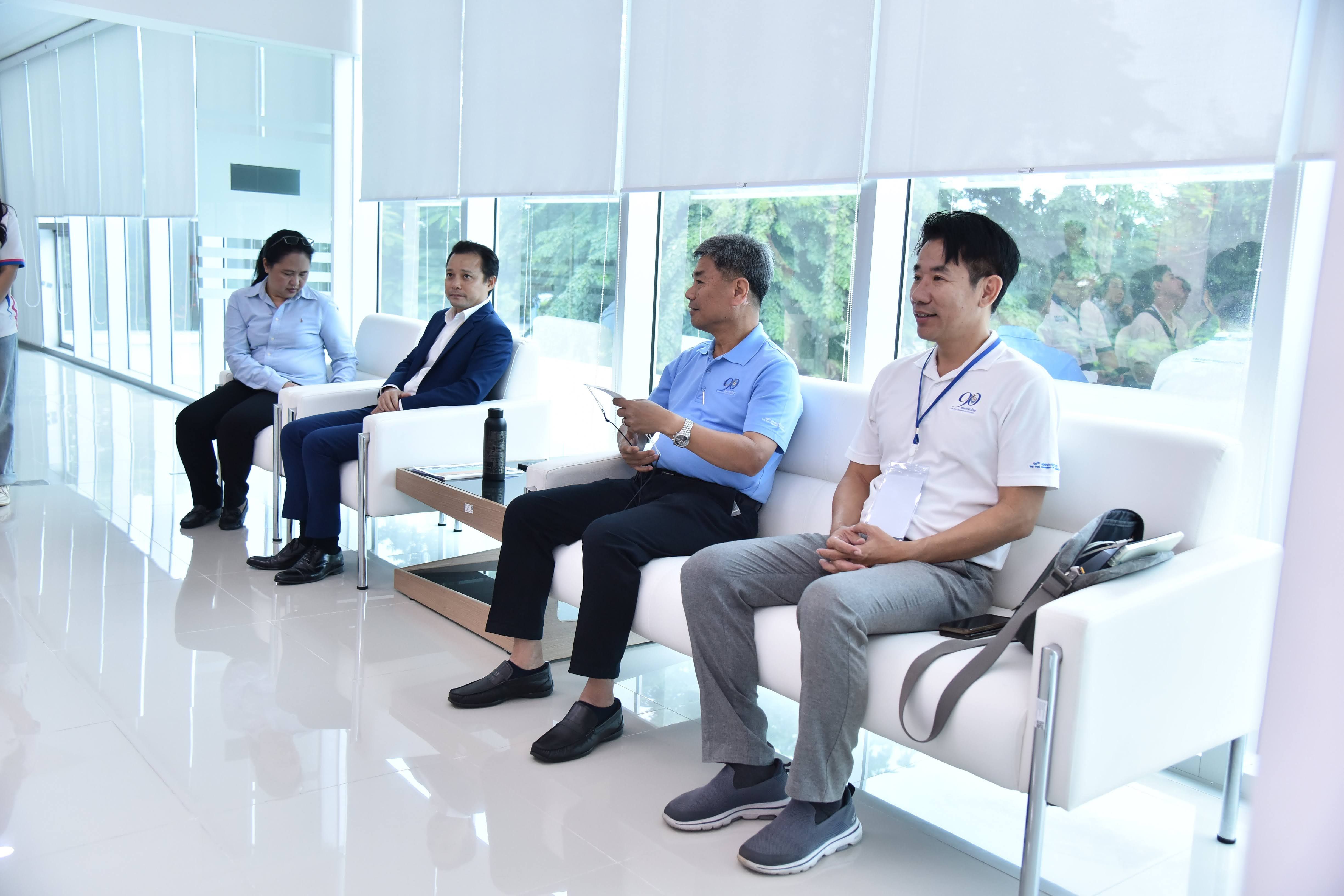 Four men sit on white couches in a modern room with large windows, engaged in discussion.