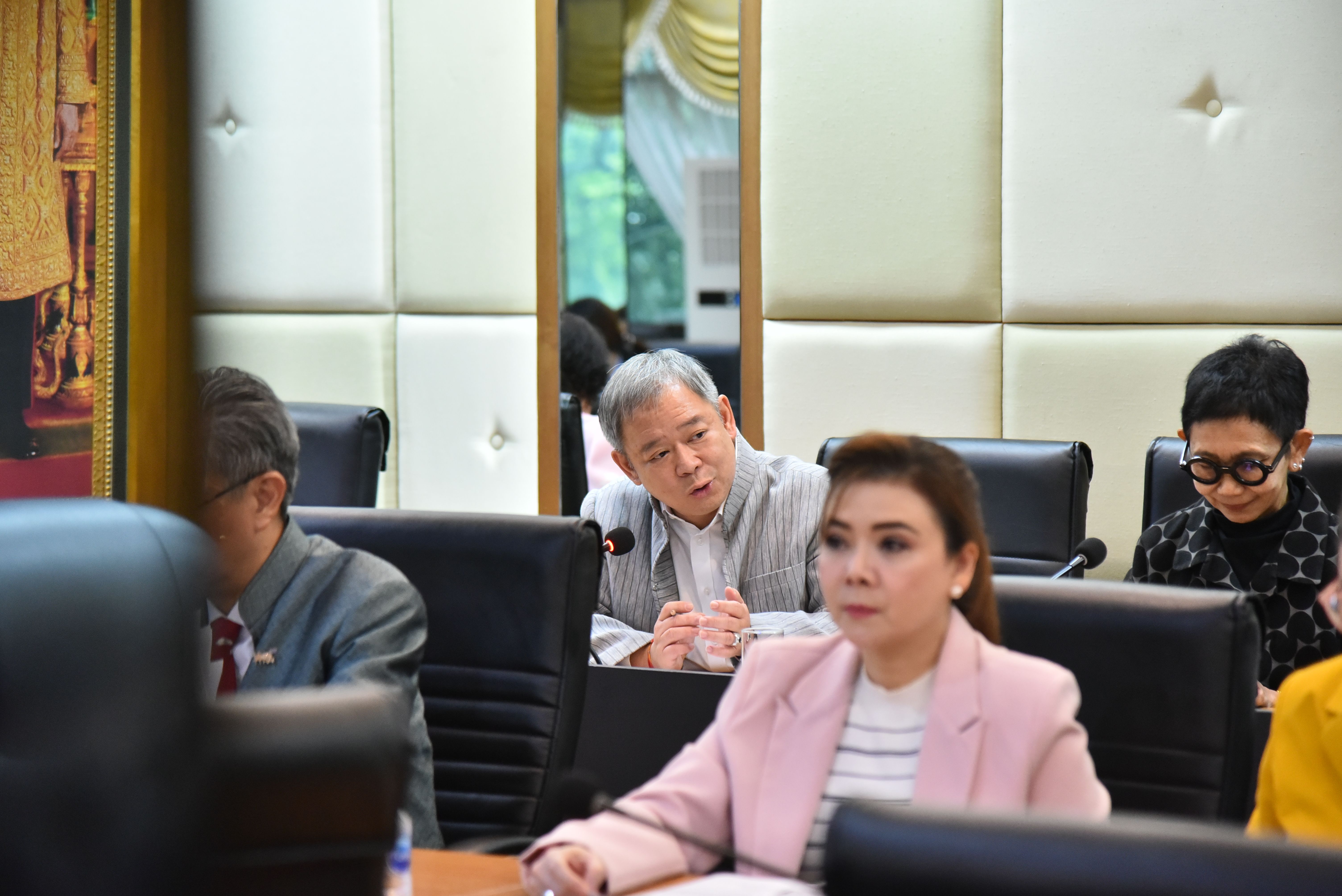 Woman in pink blazer at a conference table, with a man in grey looking on.