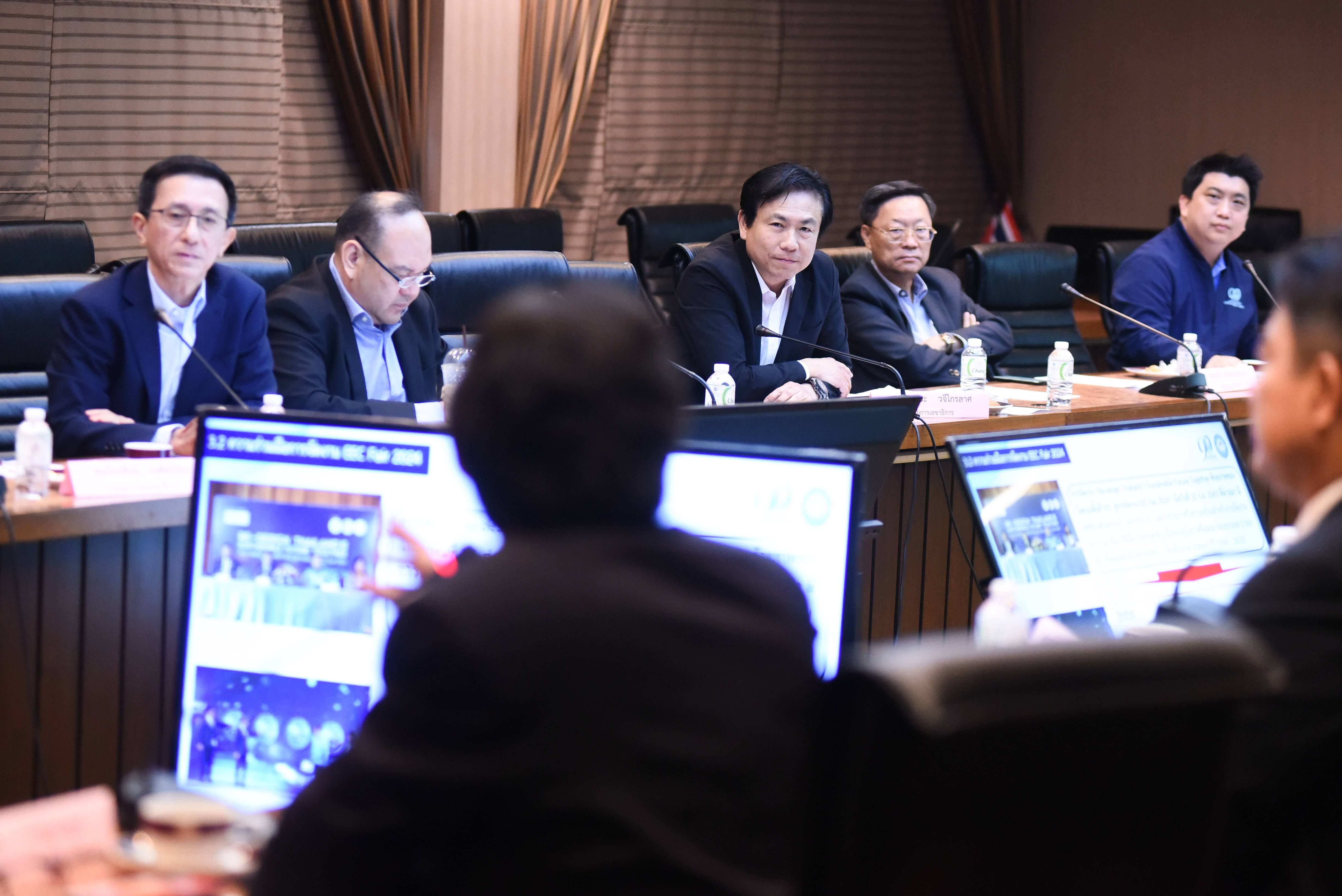 Men in a formal meeting room reviewing data on laptops during a presentation.
