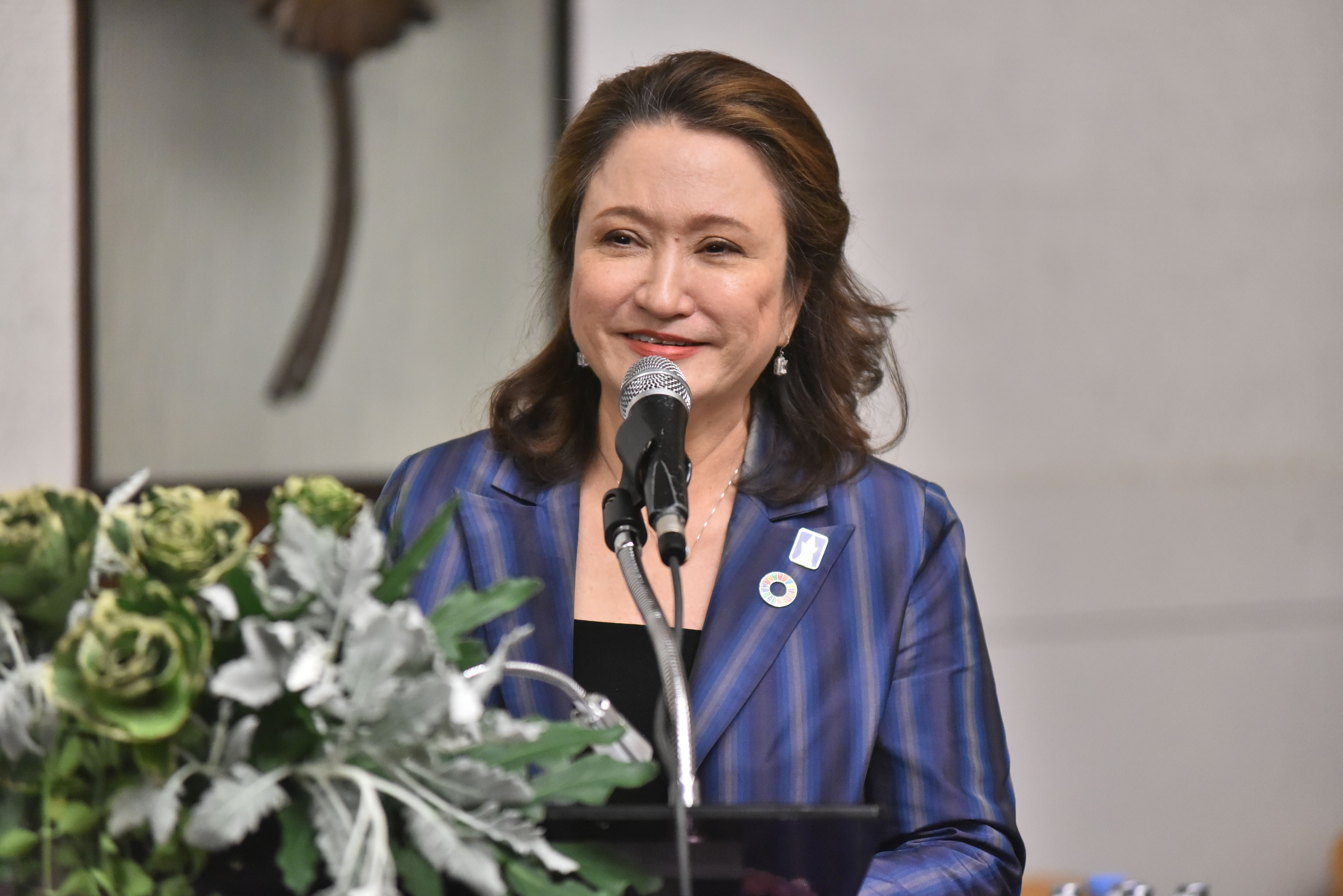 Woman in blue blazer speaking into a microphone at an indoor event.