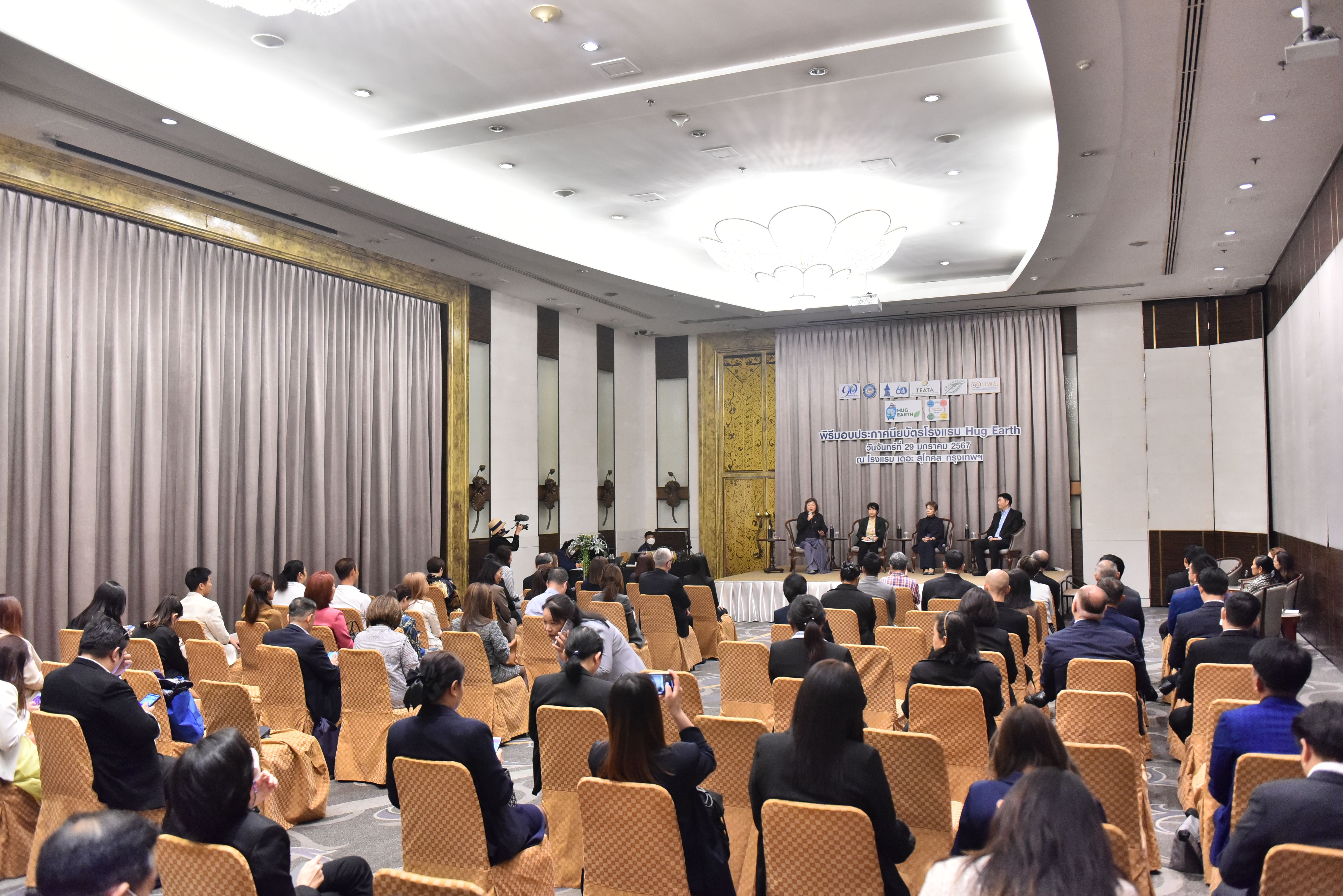Attendees listen to a panel discussion on stage in a large, elegant conference room.