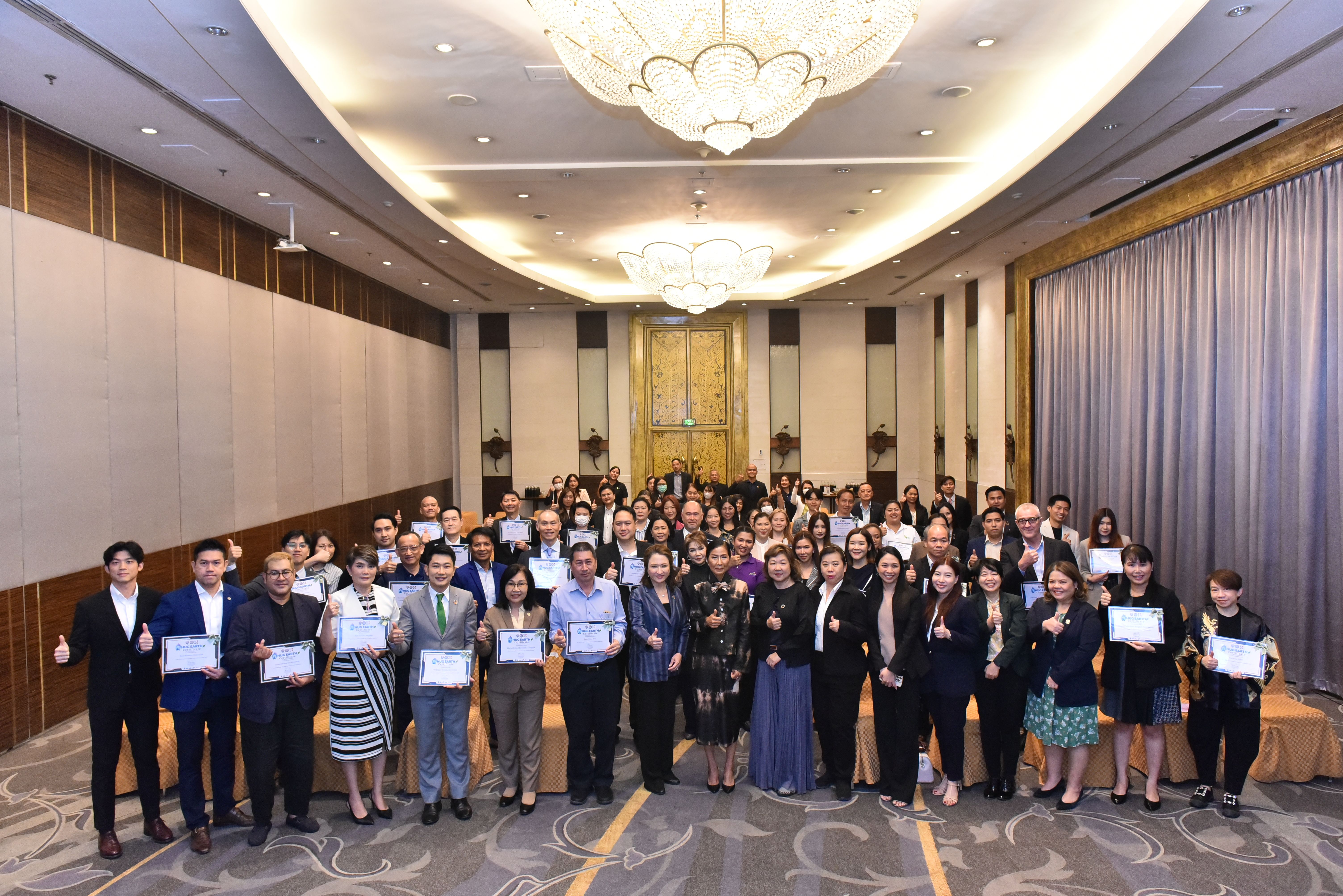 A large group of people holds certificates and awards at a formal event.