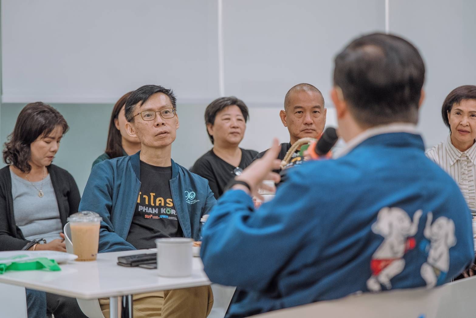 A speaker addresses a diverse group of attentive people sitting at a table.
