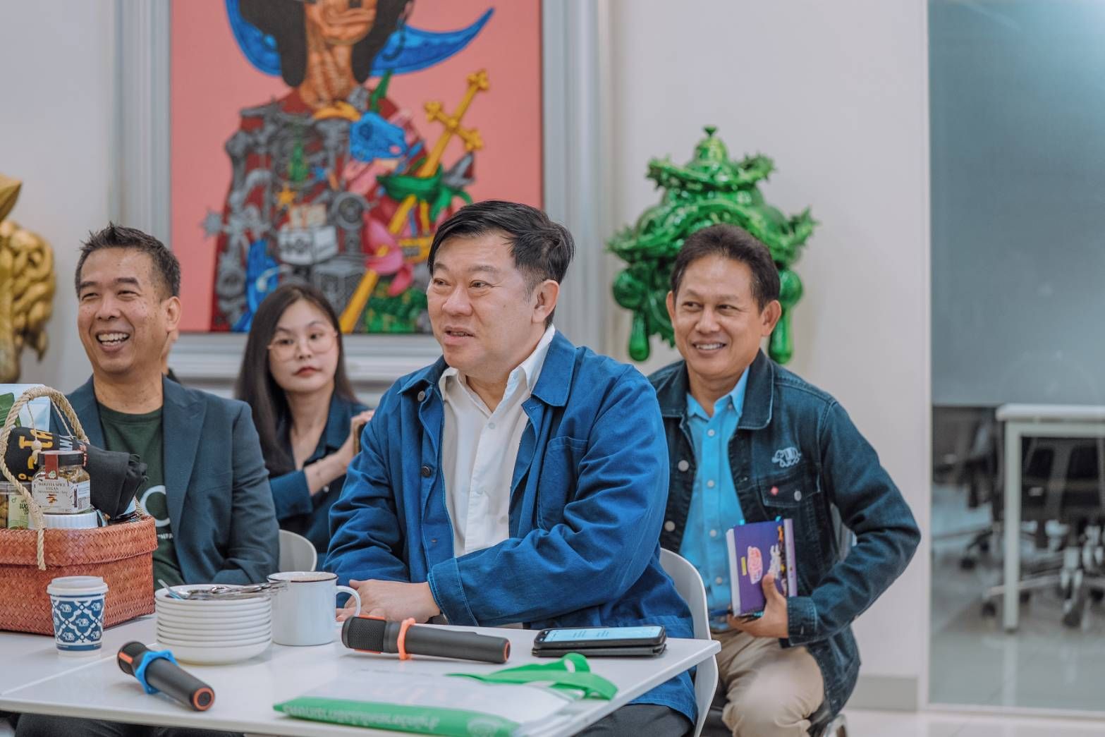 Three men seated at a table, one speaking while the others listen and smile.
