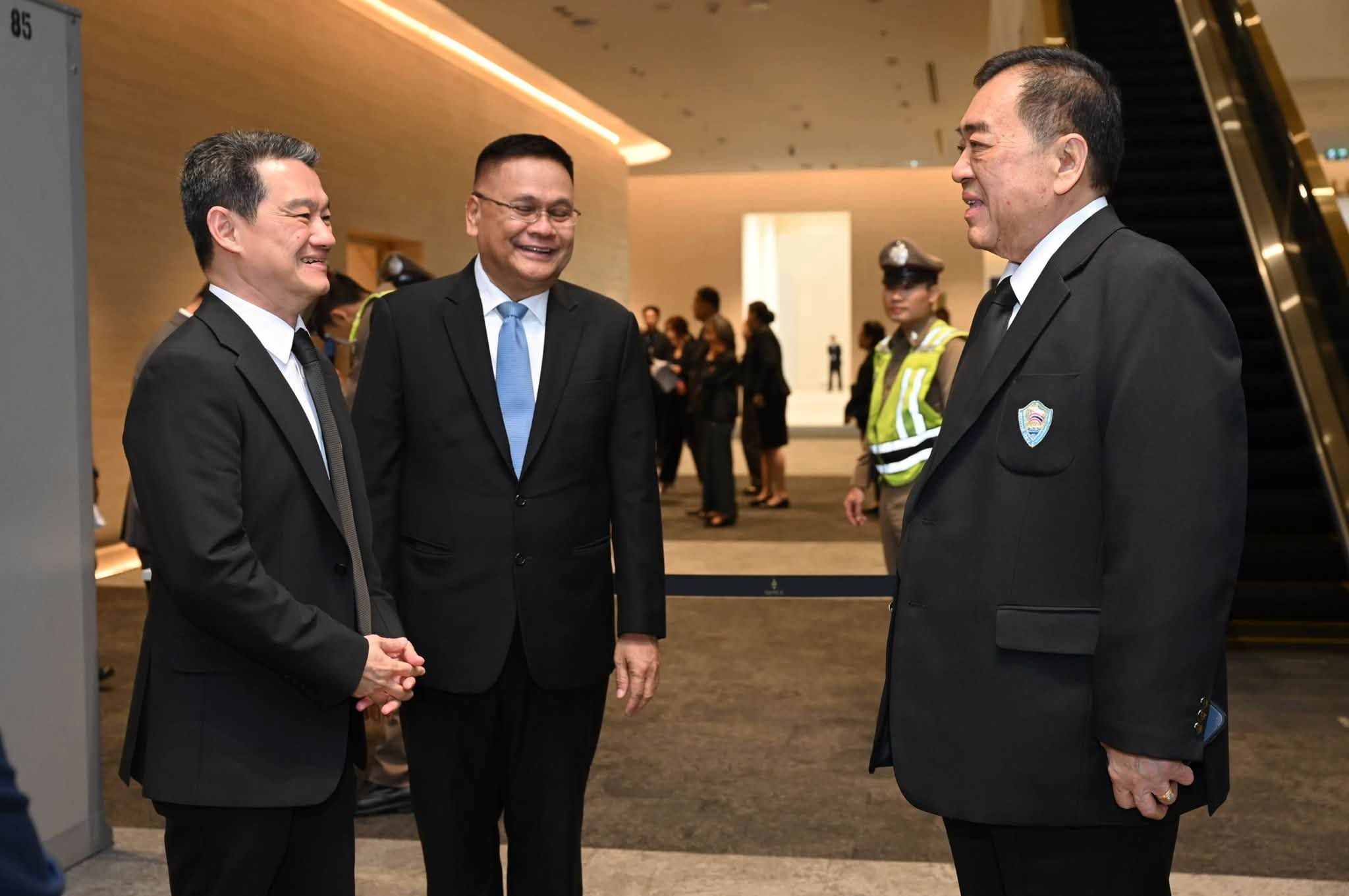 Three smiling men in dark suits converse in a modern building lobby.