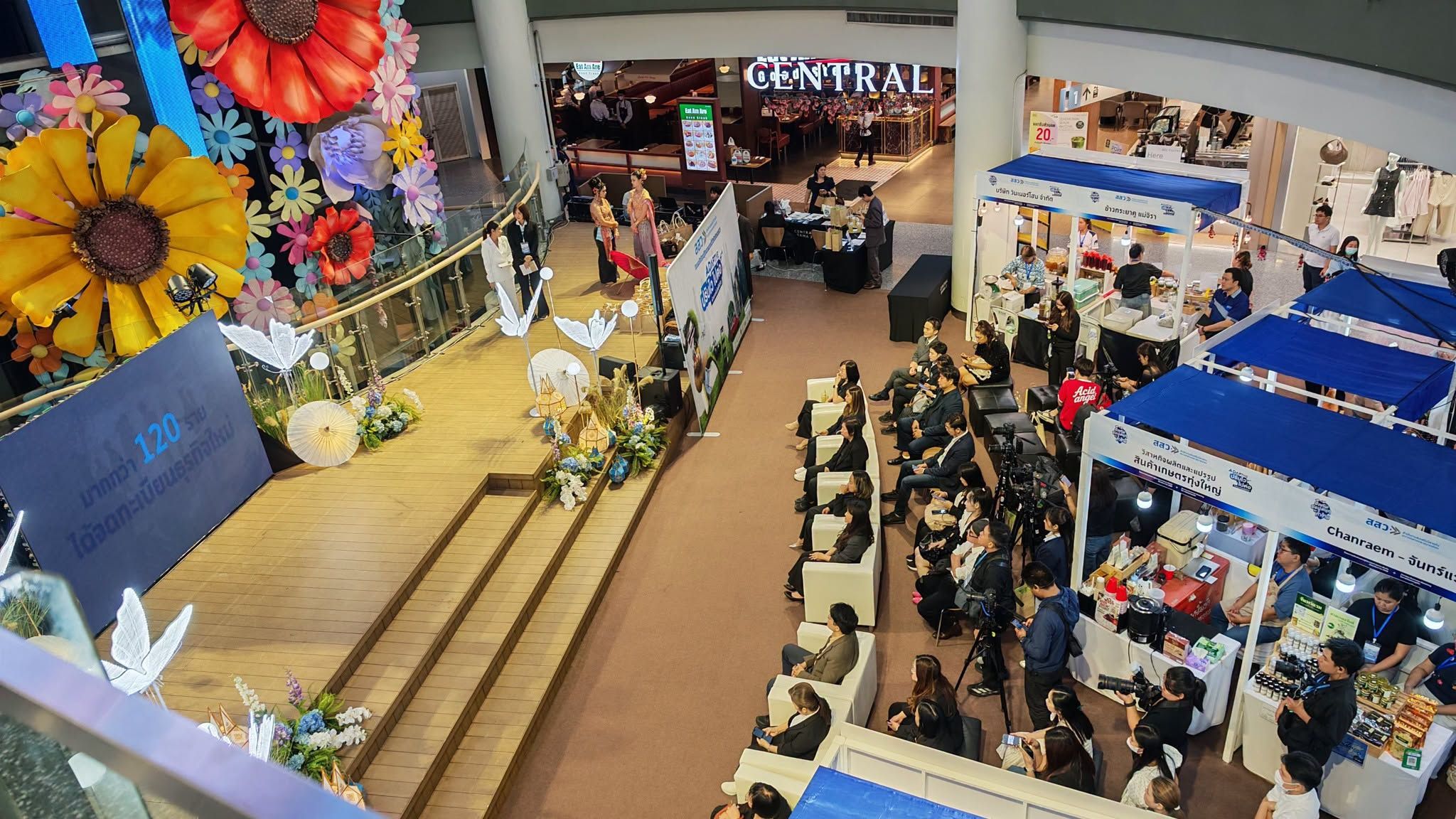 Overhead view of a bustling indoor event with a large floral stage and market stalls.