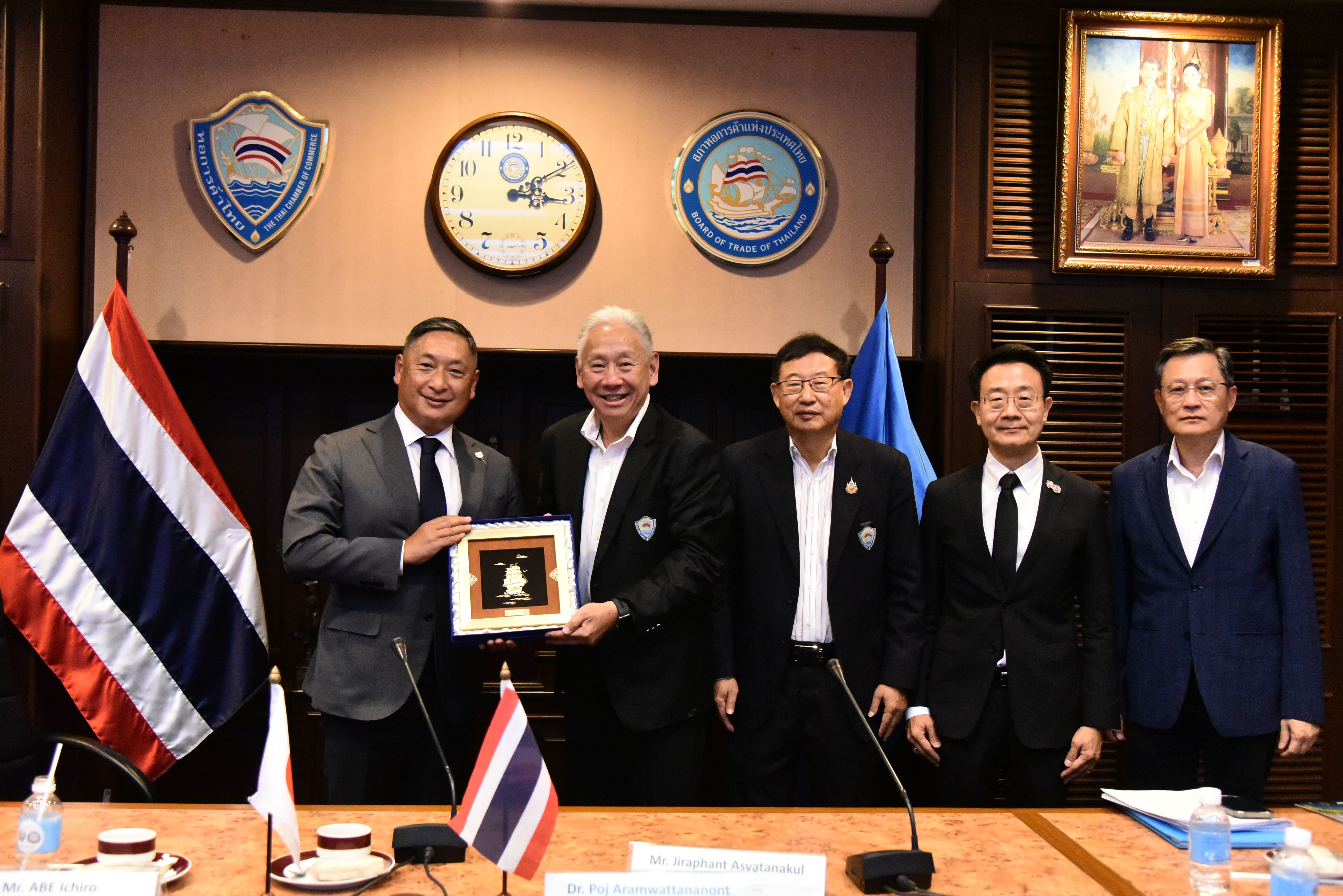 Five men in suits exchange a framed award in a formal meeting room.