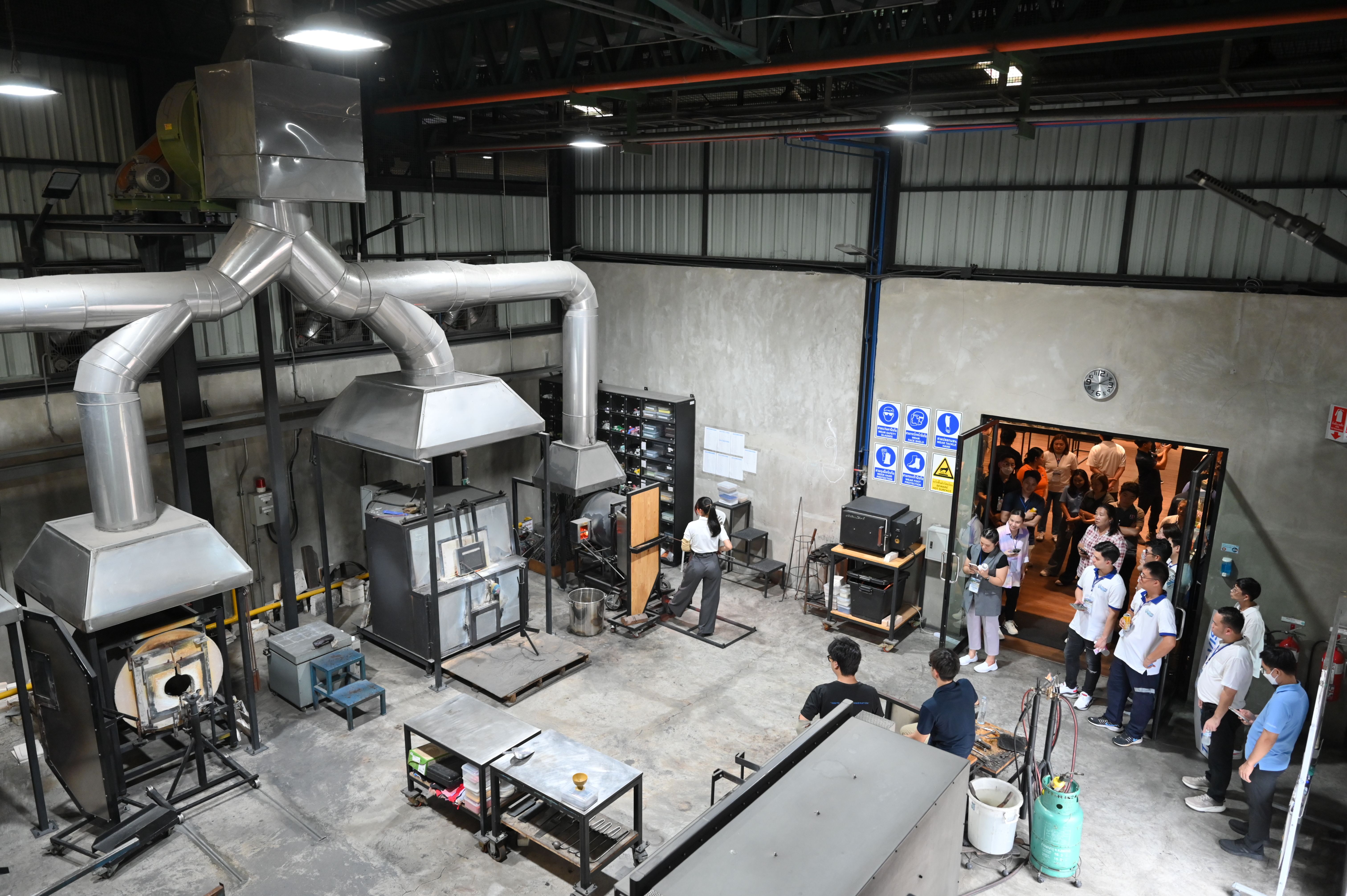 Students observe industrial machinery and equipment in a large factory workshop setting.