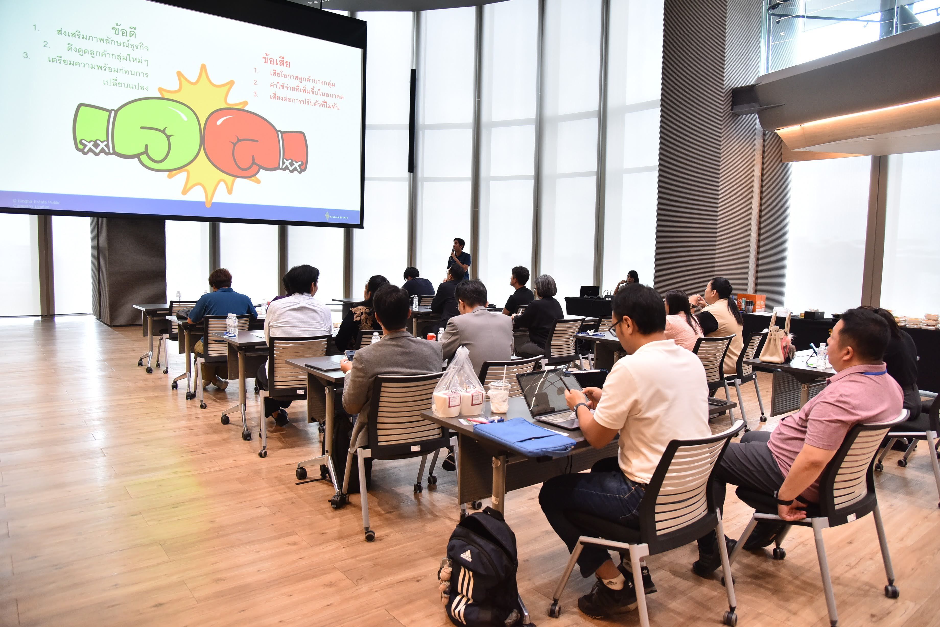 Attendees watch a presentation featuring clashing green and red boxing gloves on a large screen.