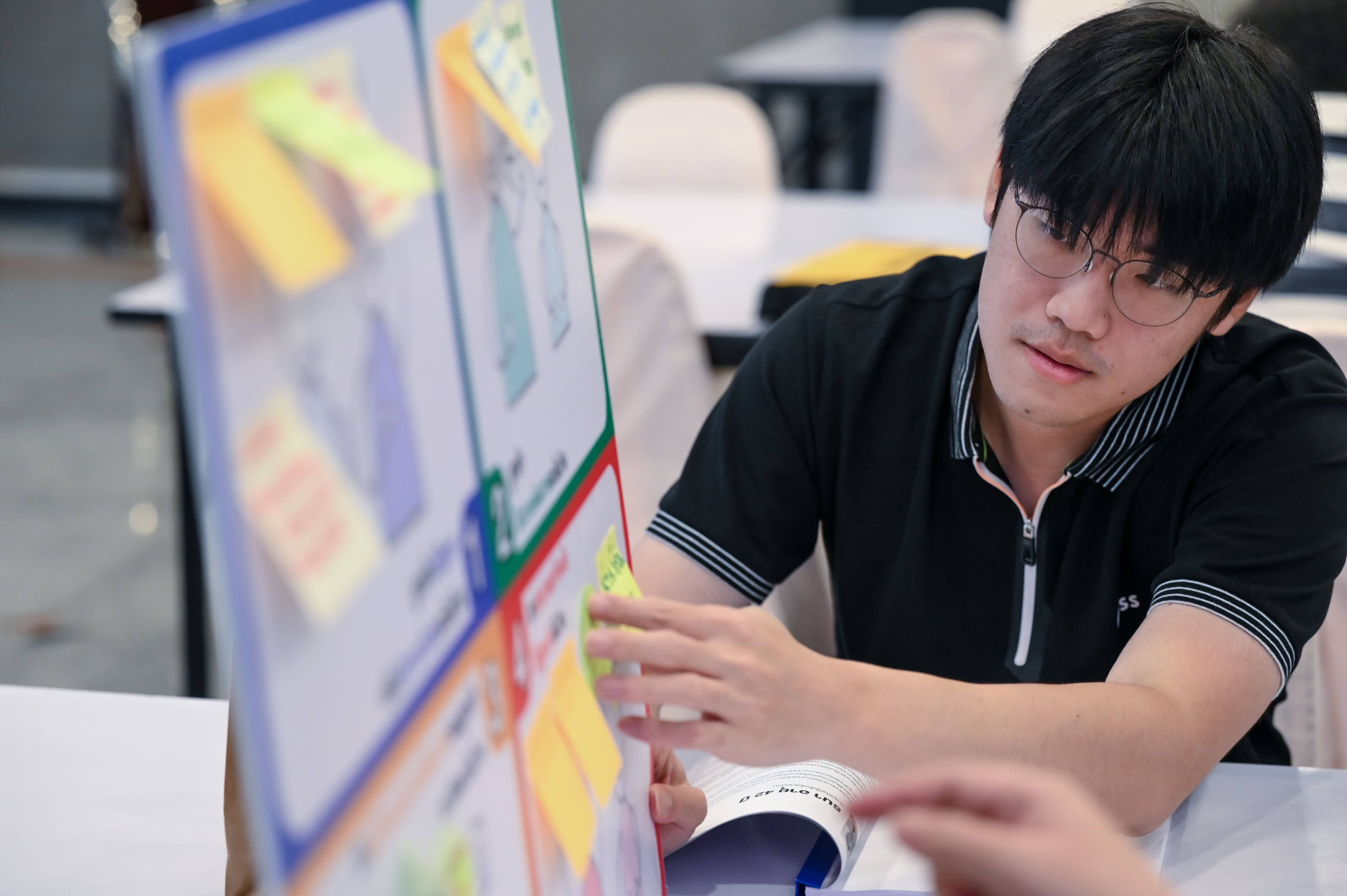 Man in glasses intently organizing colorful sticky notes on a large project board.