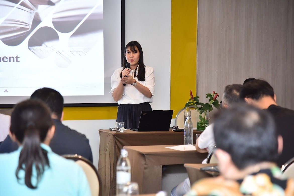 A woman presents to an audience at a conference, standing in front of a projection screen.