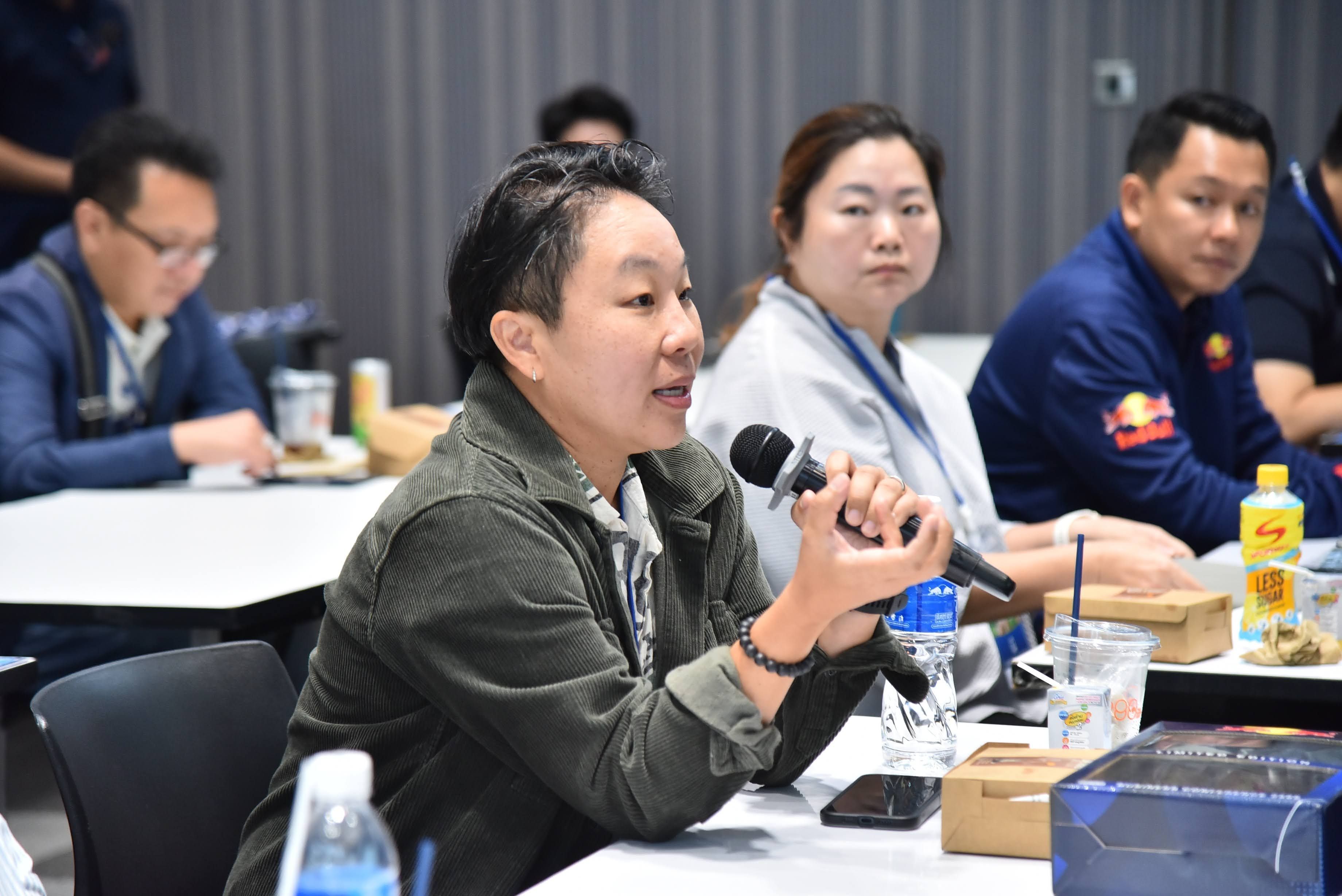 Woman in green jacket speaks into a microphone at a professional conference.