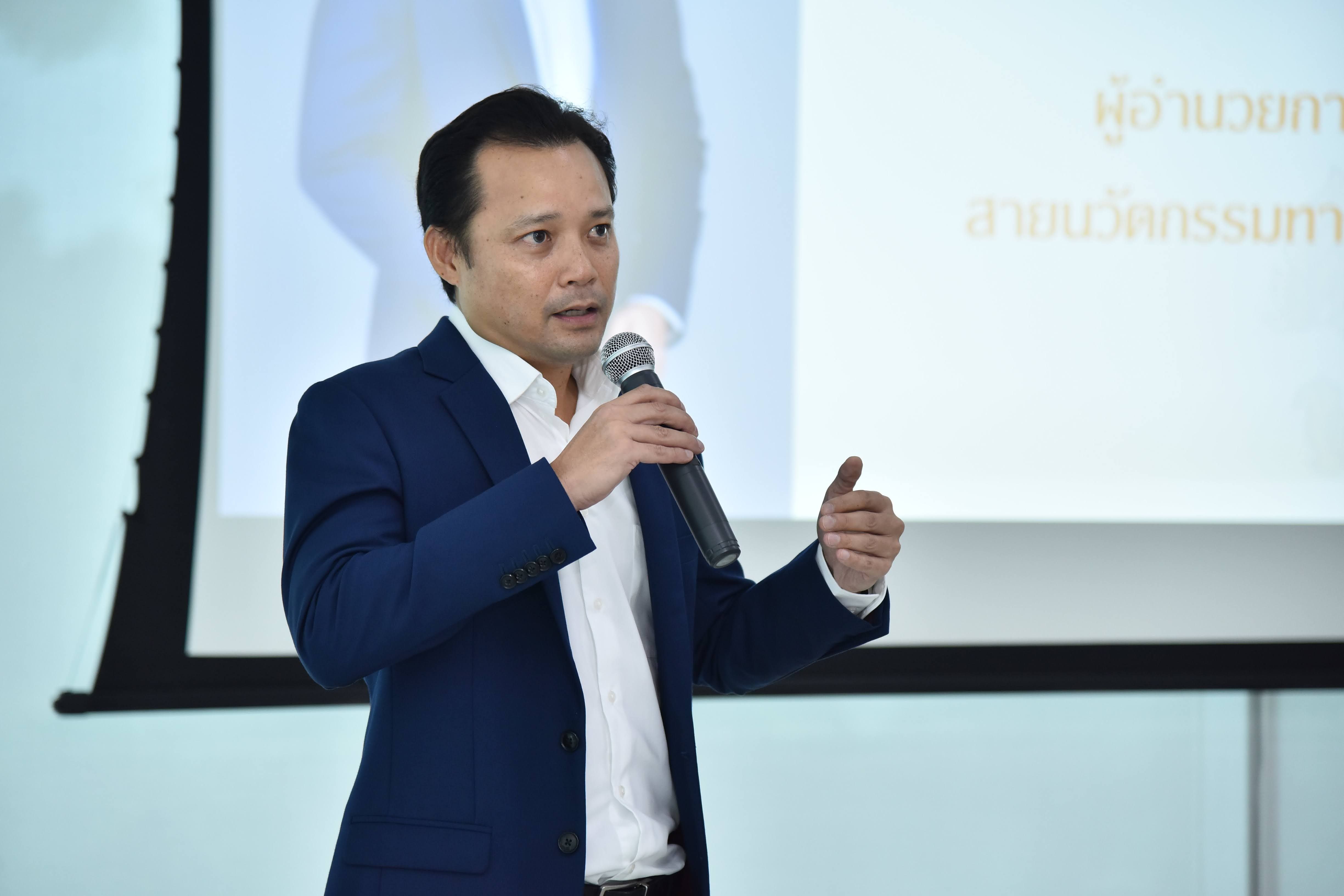 Man in blue suit speaking into microphone, gesturing during a presentation.
