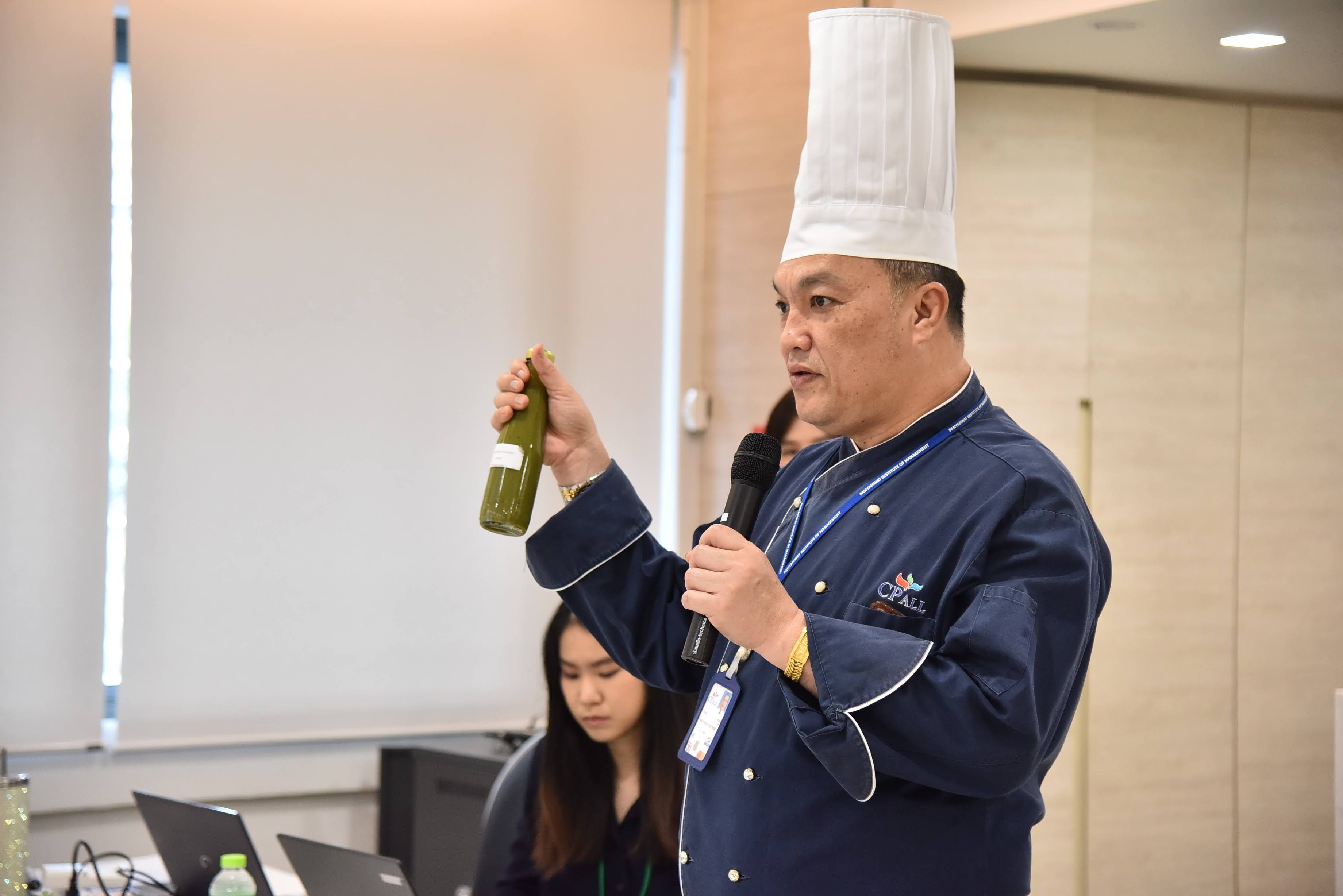 Chef demonstrates a green bottle and speaks into a microphone during a culinary presentation.