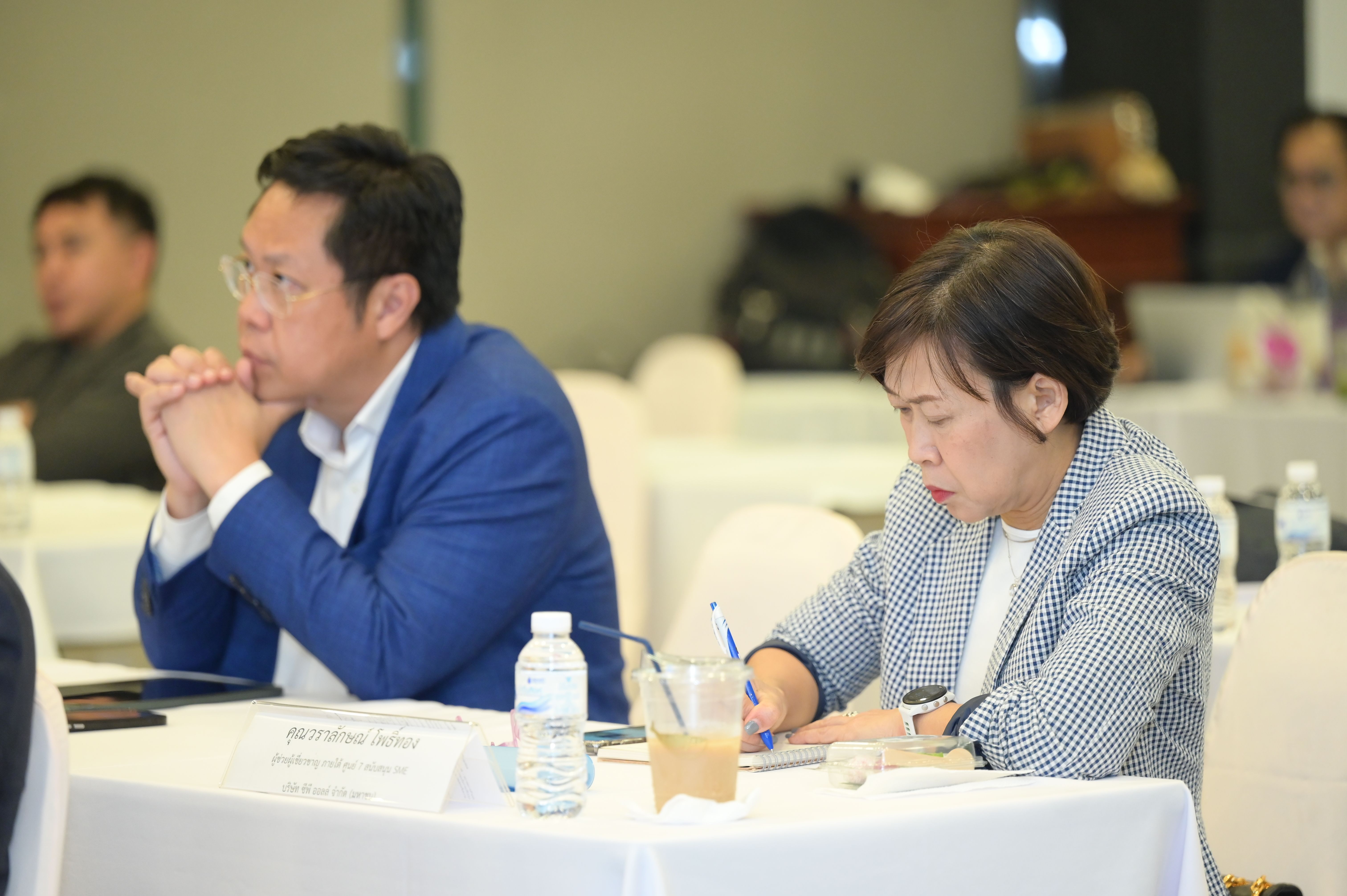 A man listens intently while a woman takes notes at a professional meeting.