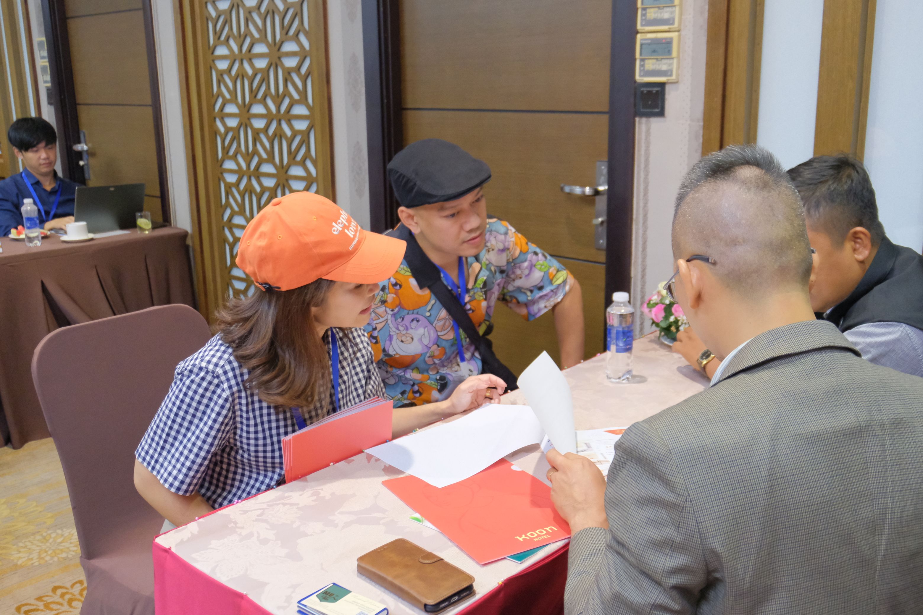 Woman in orange hat and man in black cap review documents at a meeting table.
