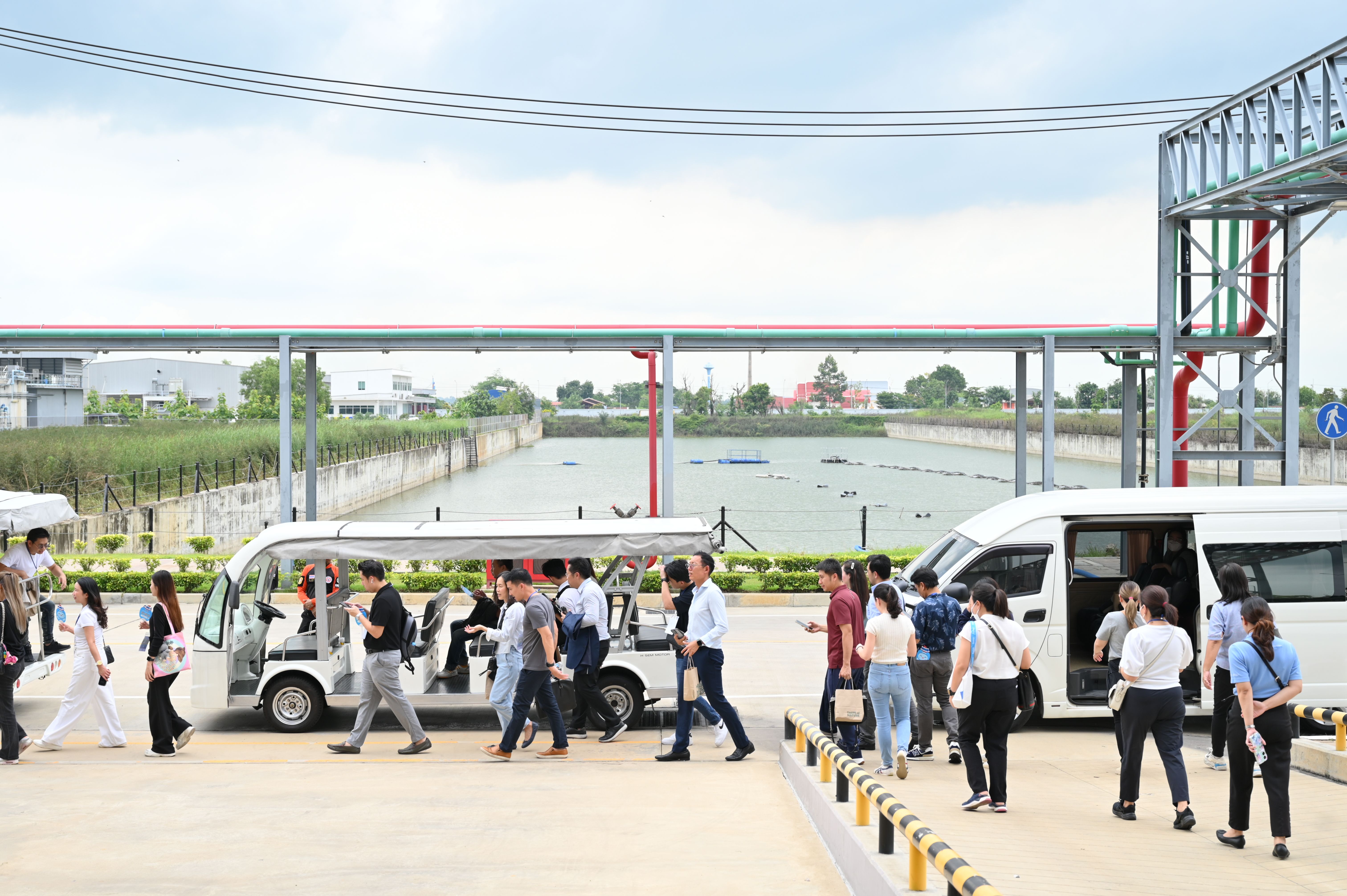 People disembarking from a shuttle bus and golf cart at an industrial site.