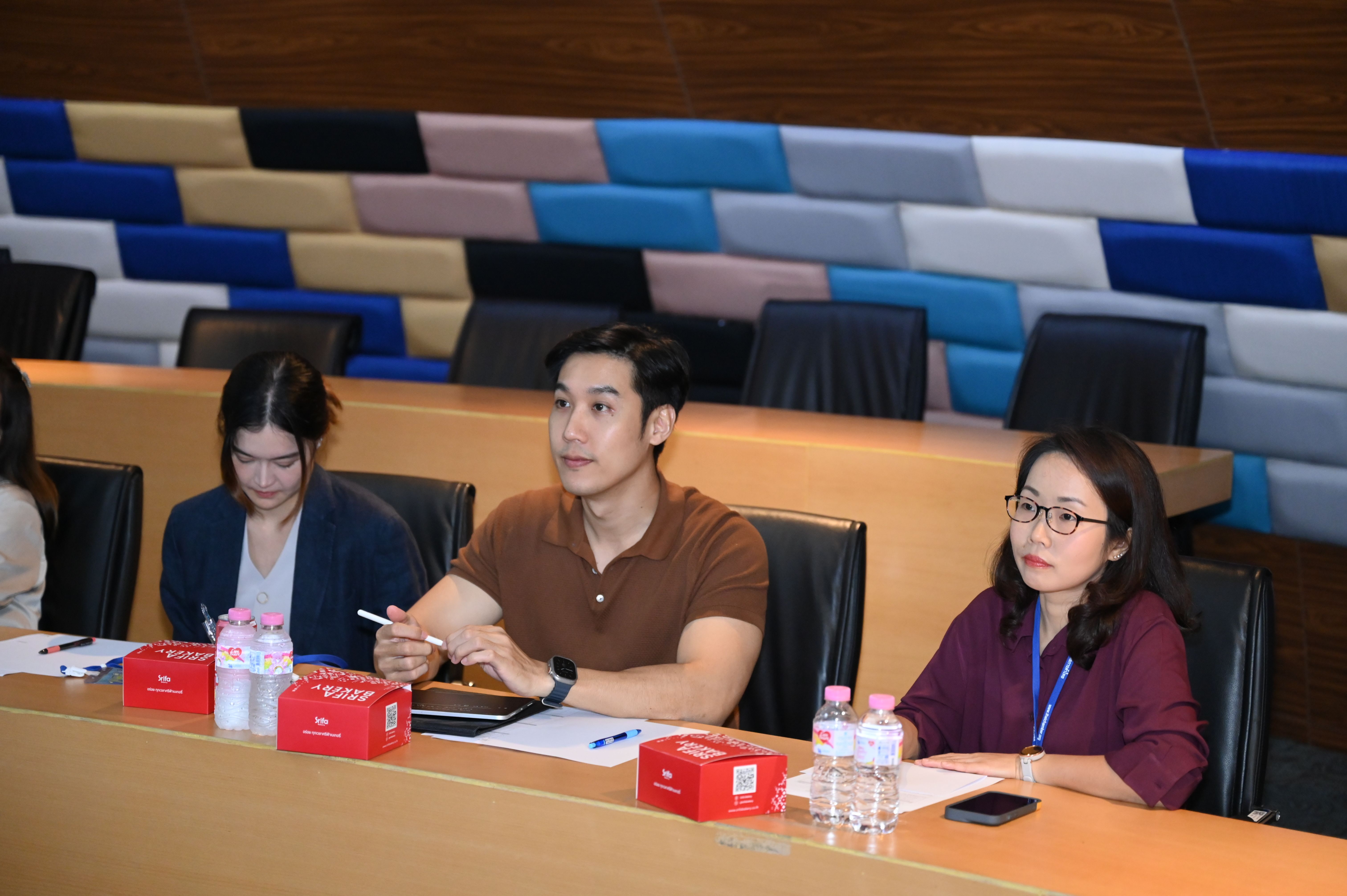 Three professionals attentively listening in a modern conference room with colorful wall panels.
