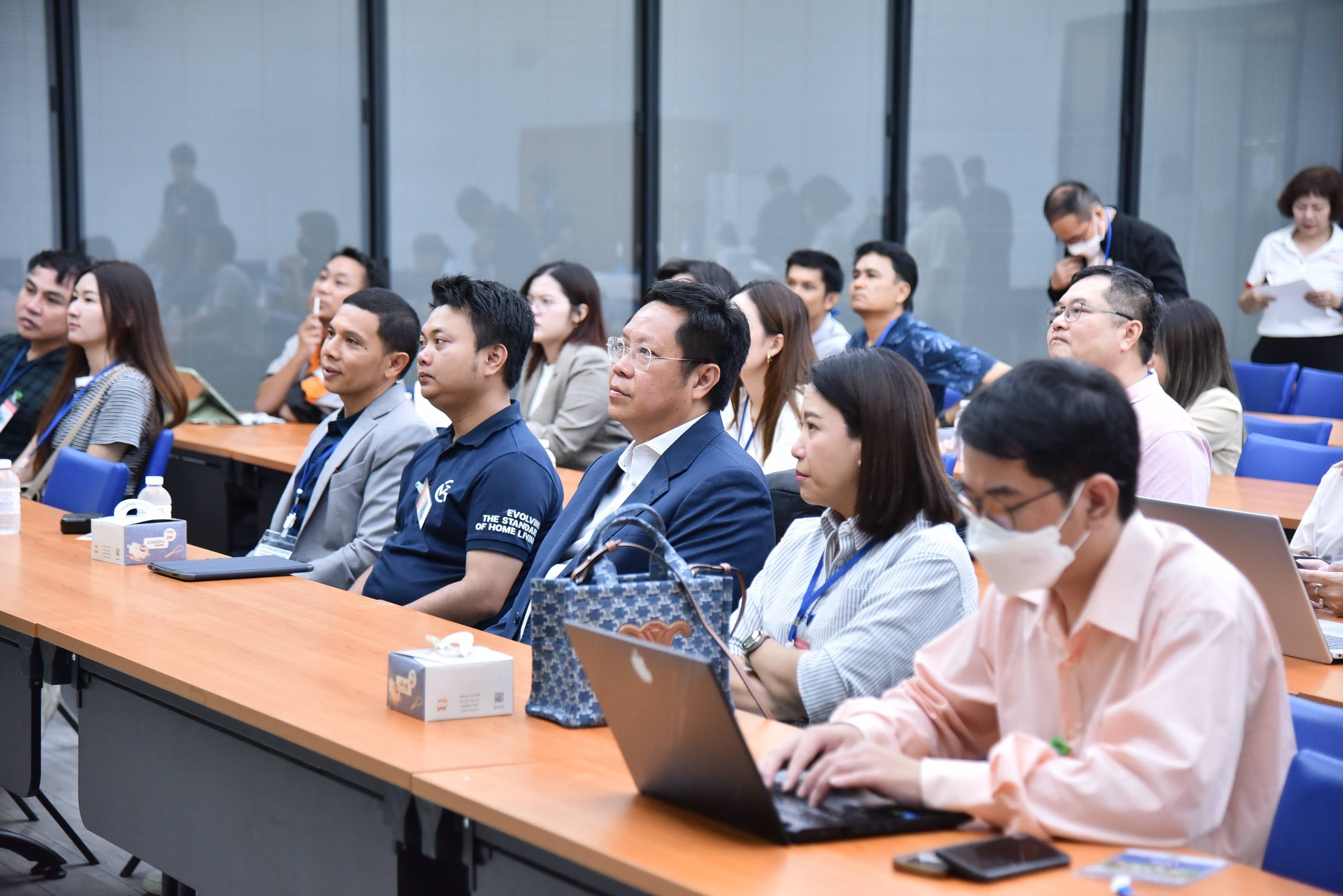 Professionals attend a presentation in a modern conference room, some engaged with laptops.