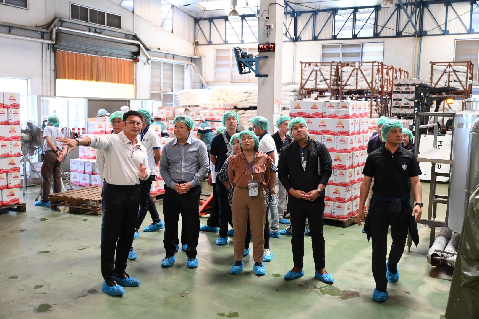 A group of people wearing hairnets and shoe covers touring a factory production area.