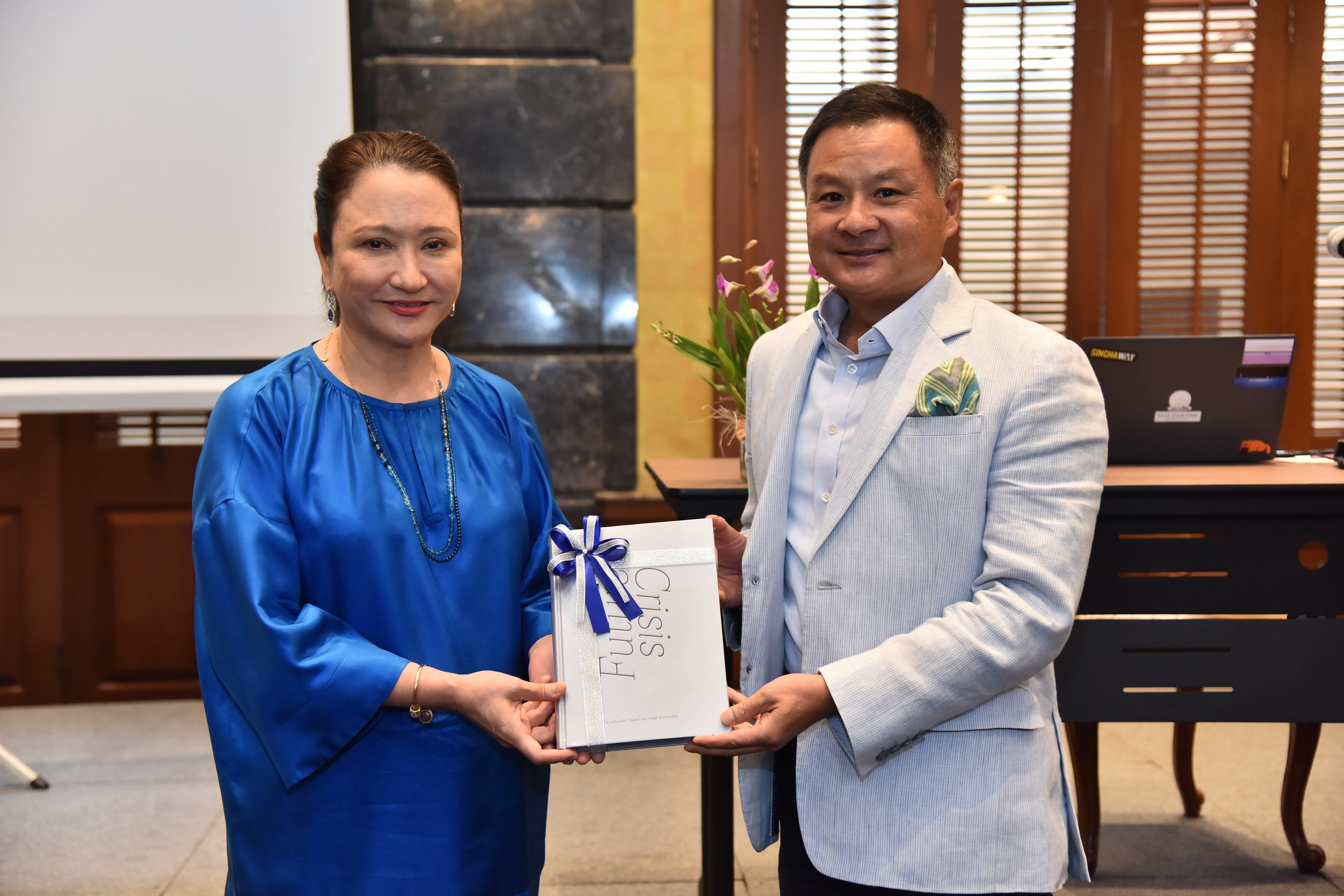 Woman in blue dress presents formal document to man in light suit at a professional event.