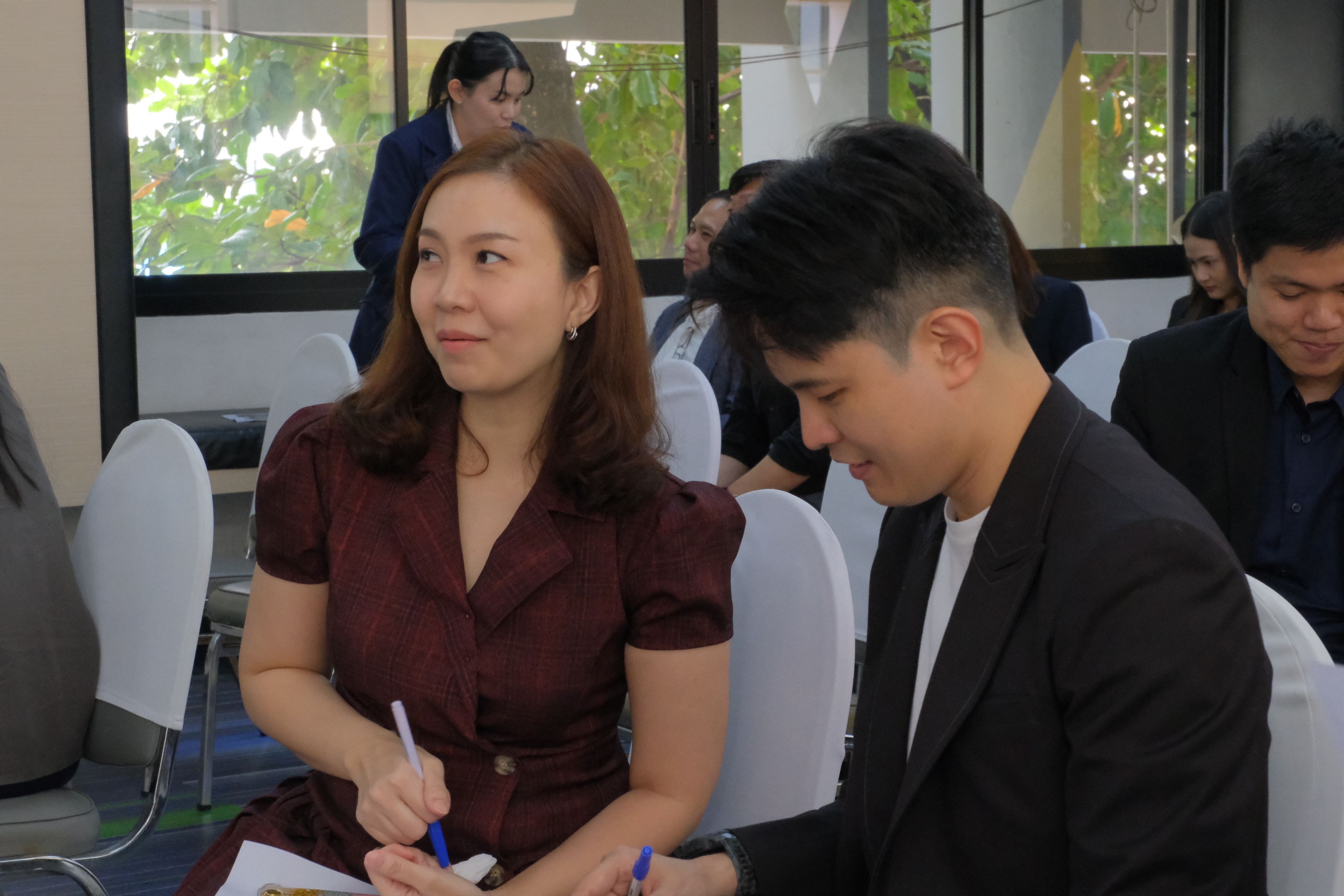 Woman in maroon dress and man in suit taking notes at a professional event.