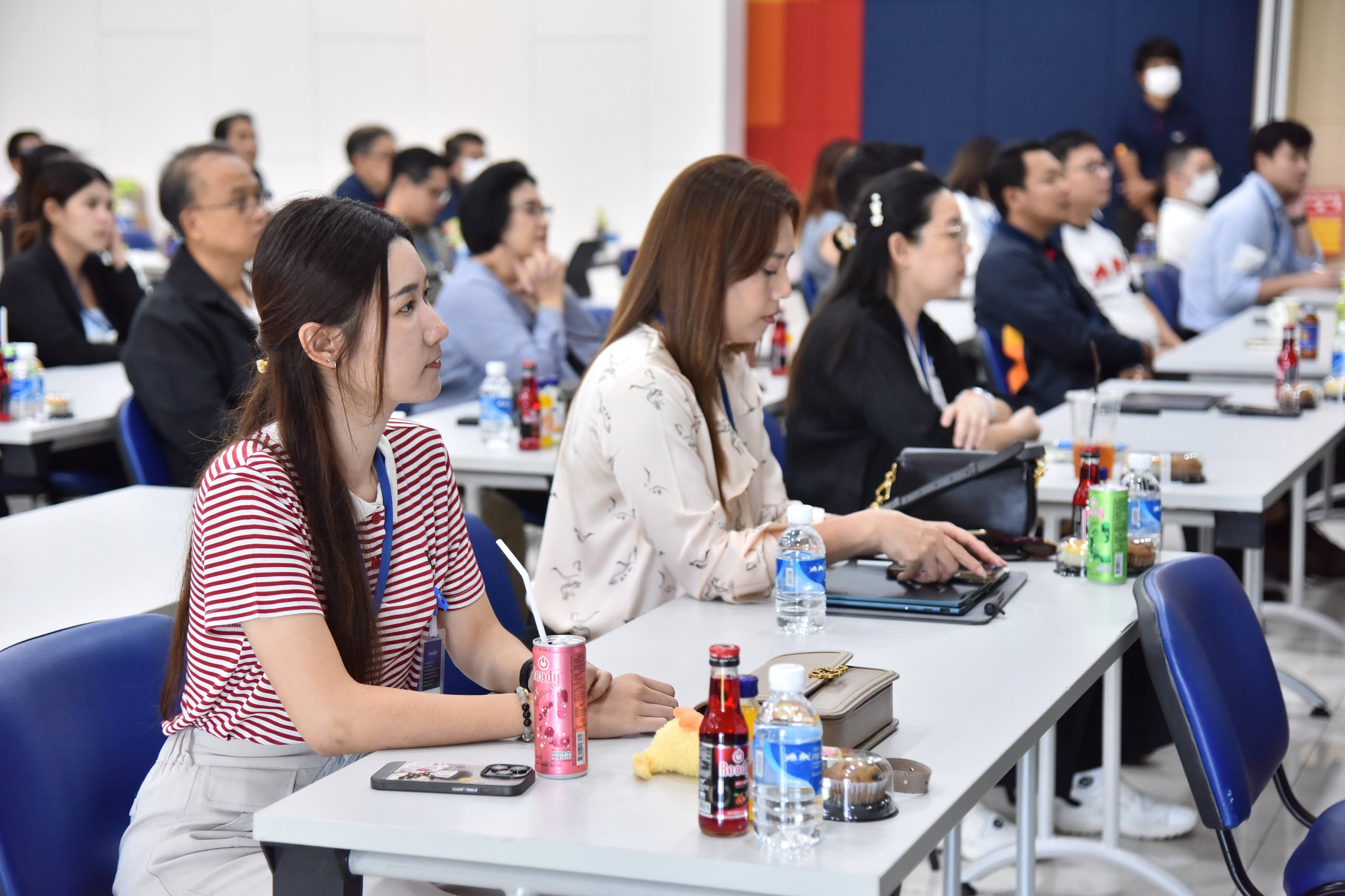 A group of diverse attendees sits at tables, attentively listening during a seminar.