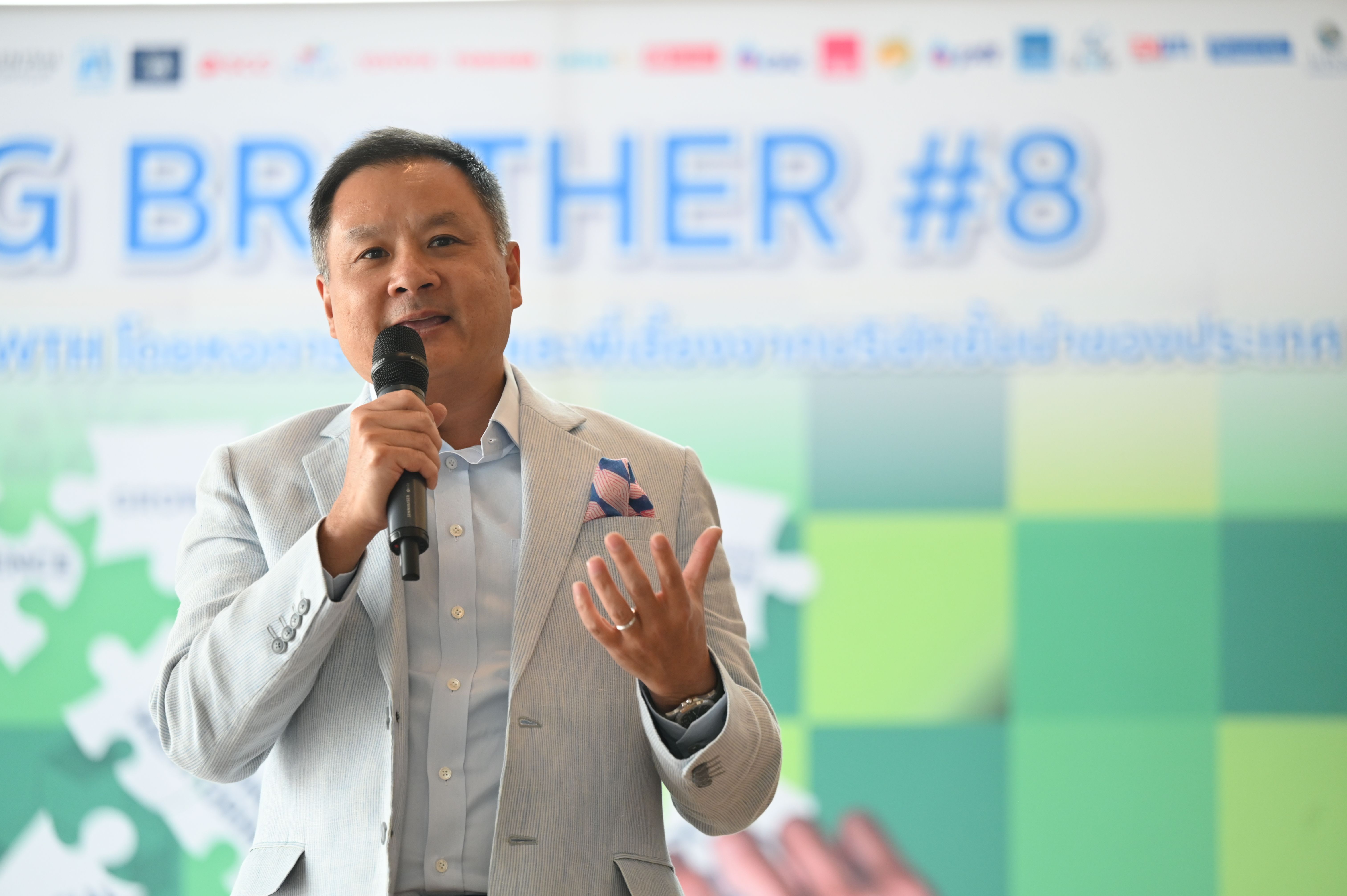 An Asian man in a light suit speaks into a microphone at an event.