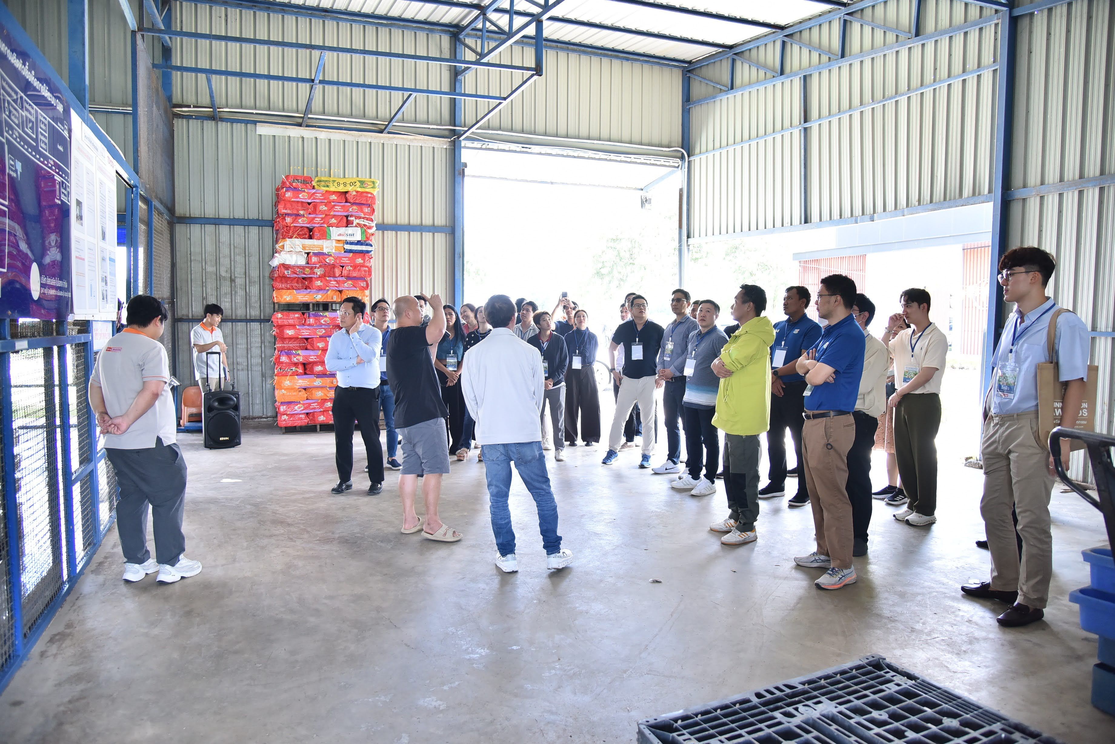 A group of people attending a presentation inside a large warehouse with stacked boxes.