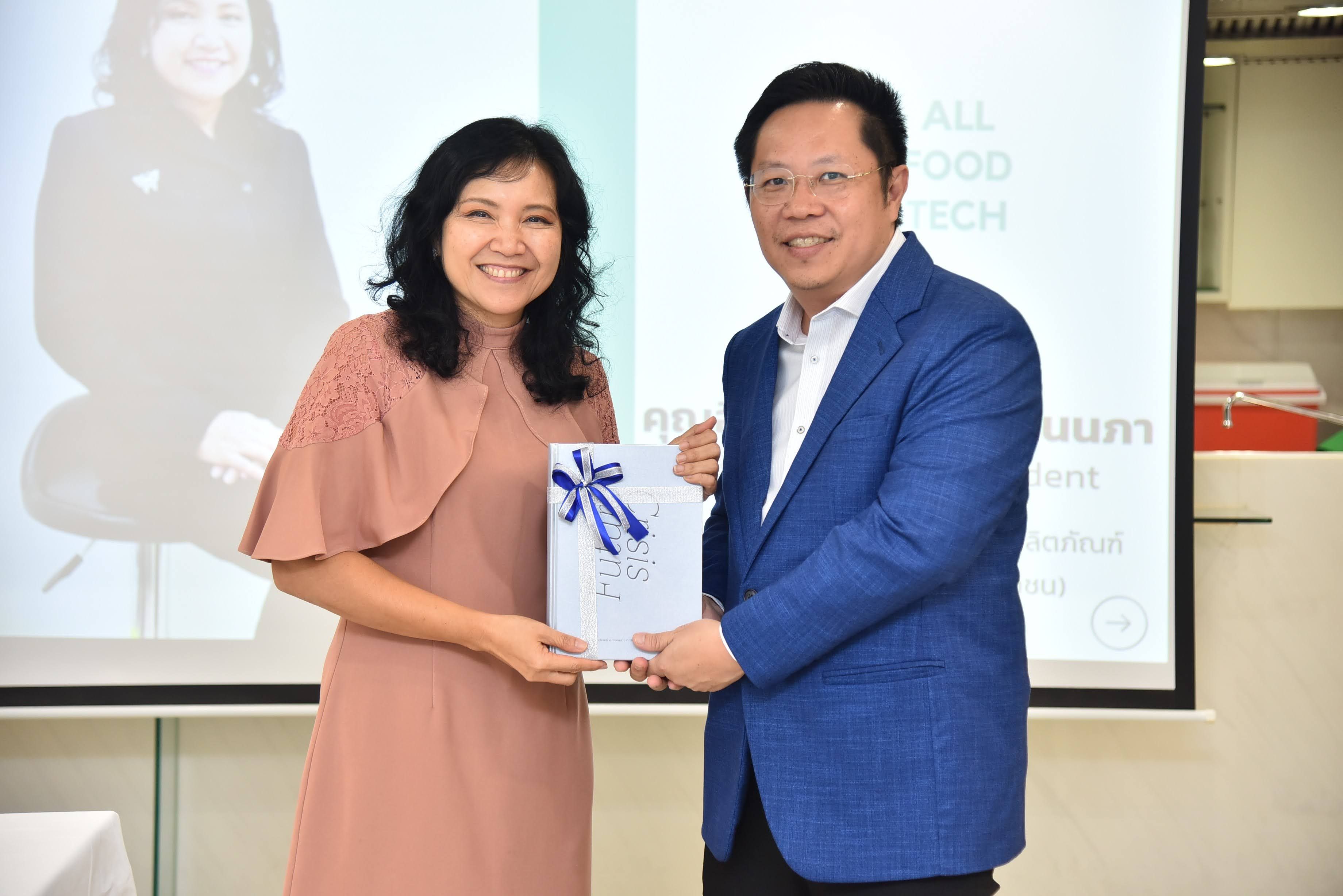Smiling man in blue suit and woman in pink dress exchanging a gift.