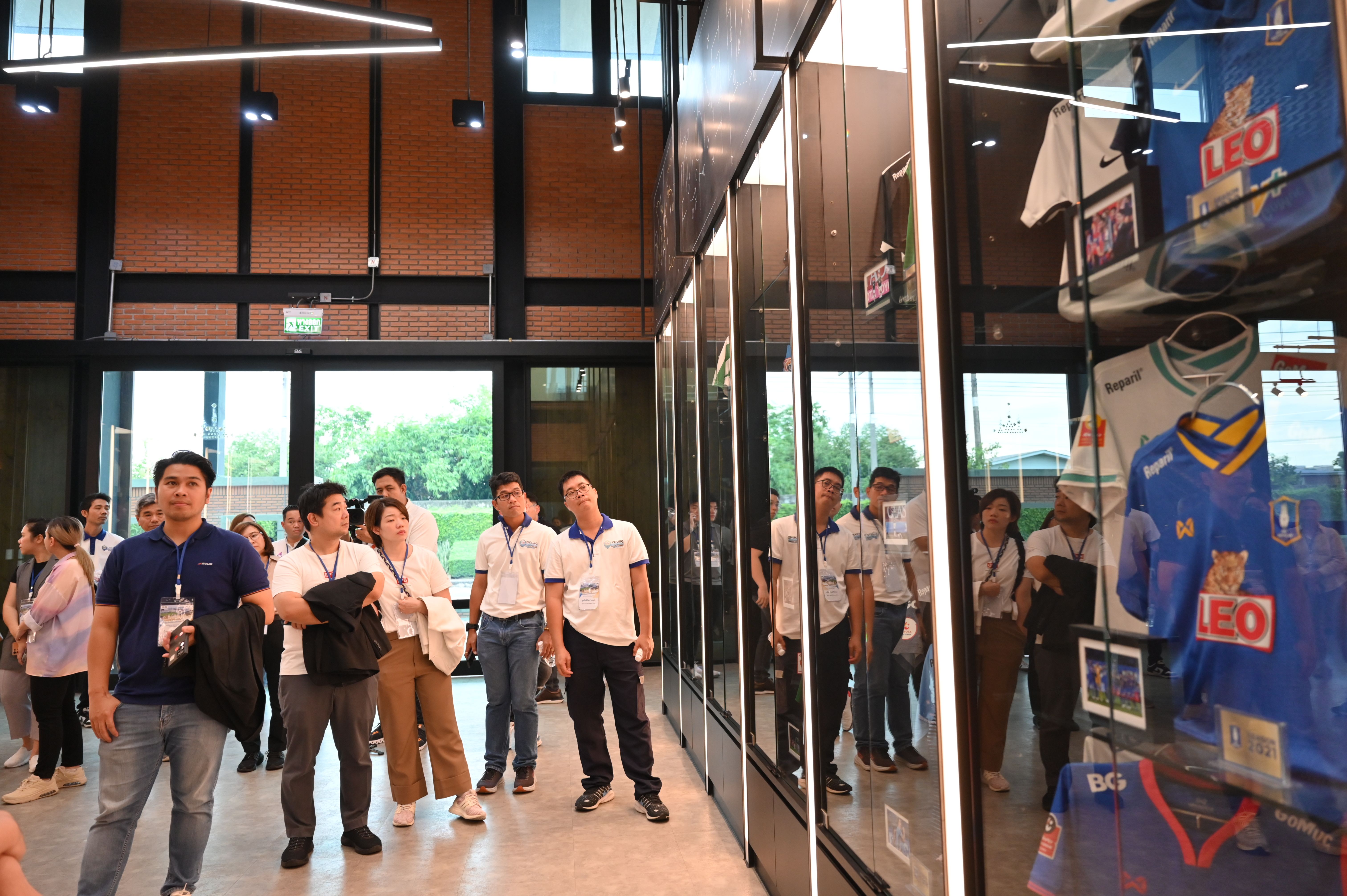 Visitors observe football jerseys displayed in a sleek glass case inside a modern hall.