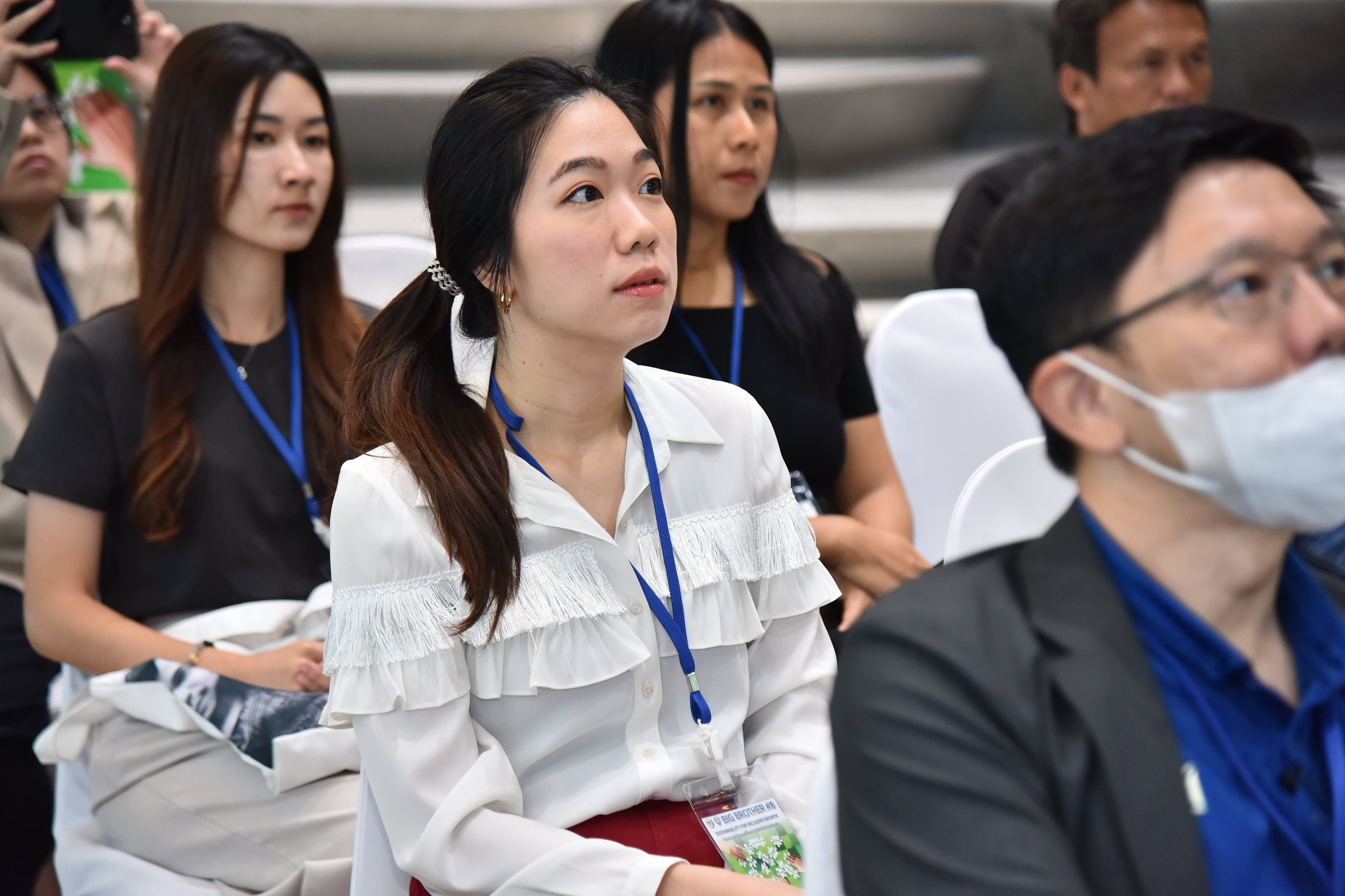 Young woman in white ruffled blouse and blue lanyard attentively watches a presentation.