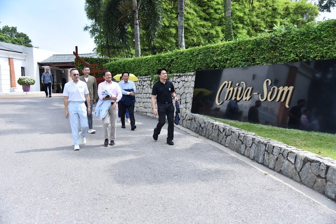 Group of people walking past a Chiva Som sign at a resort entrance.