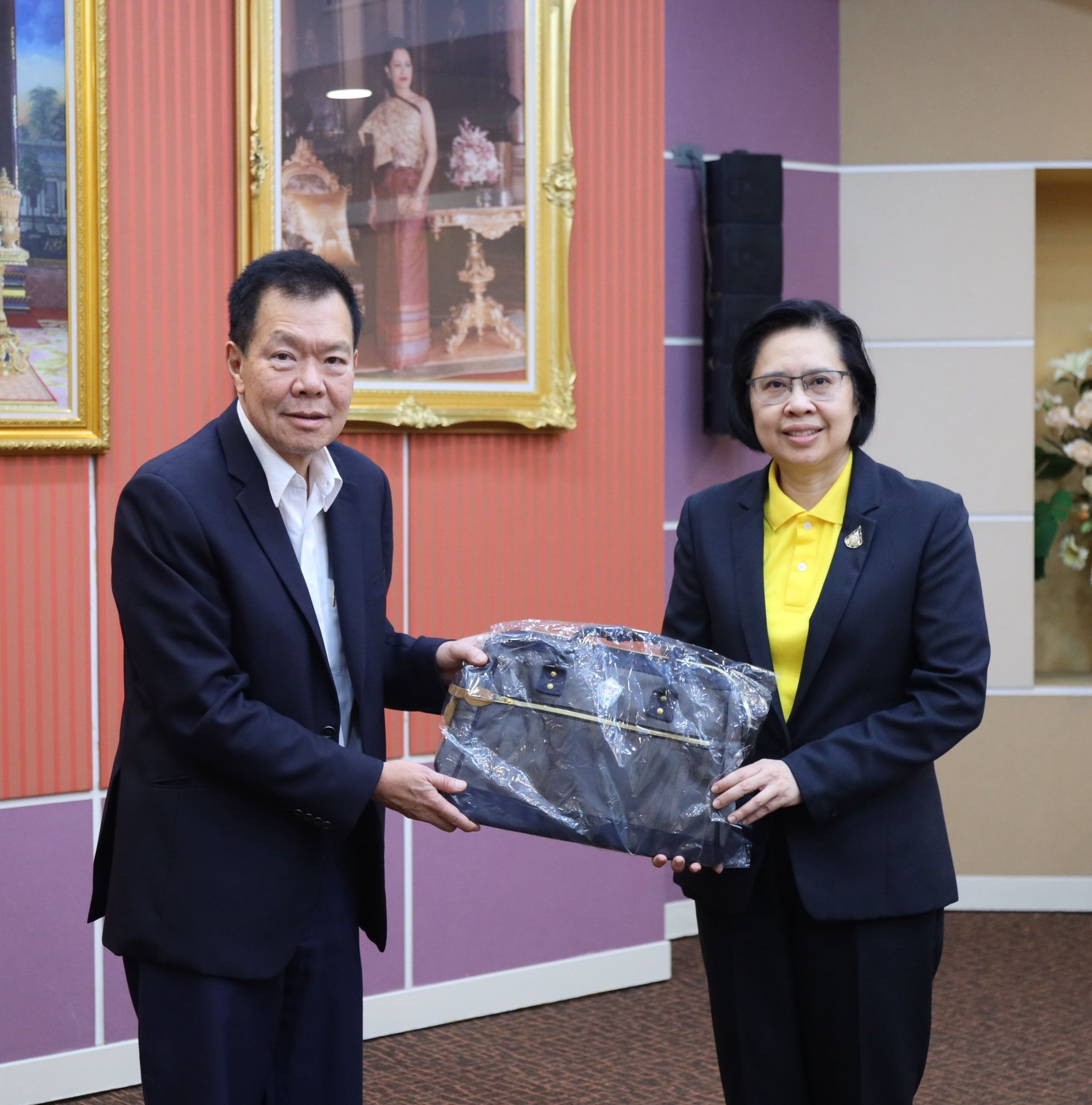 A man in a dark suit and a woman in a yellow shirt exchange a package.