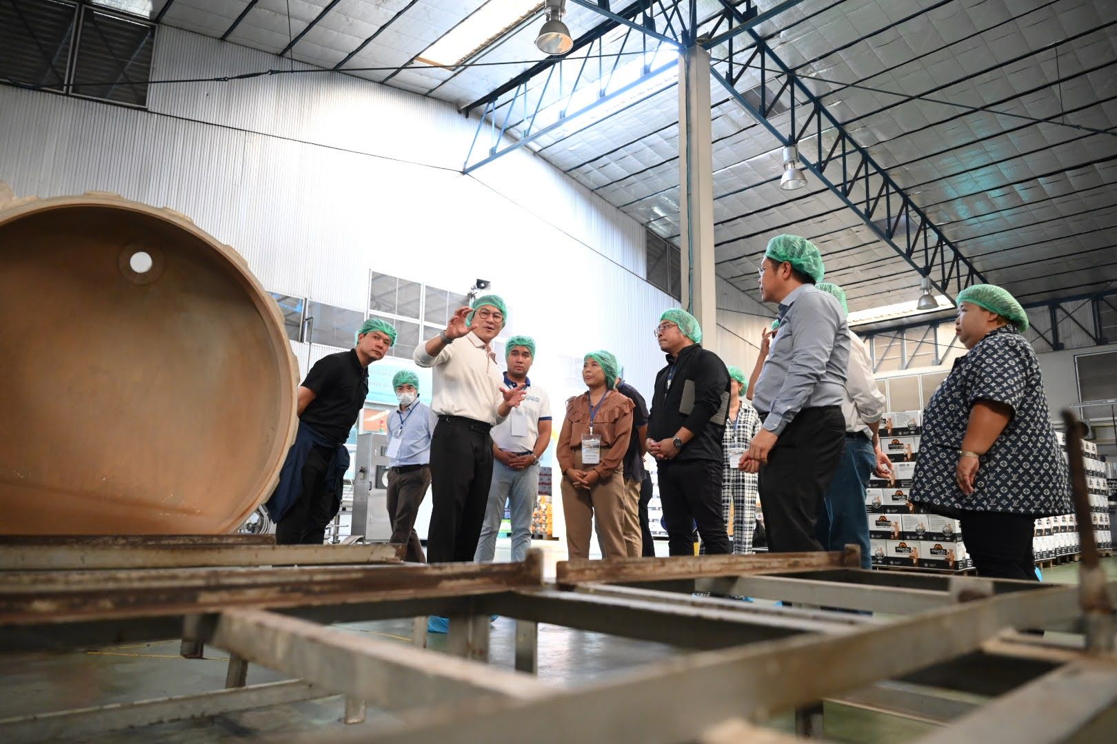 A group of people wearing hairnets tours an industrial factory, observing large machinery.