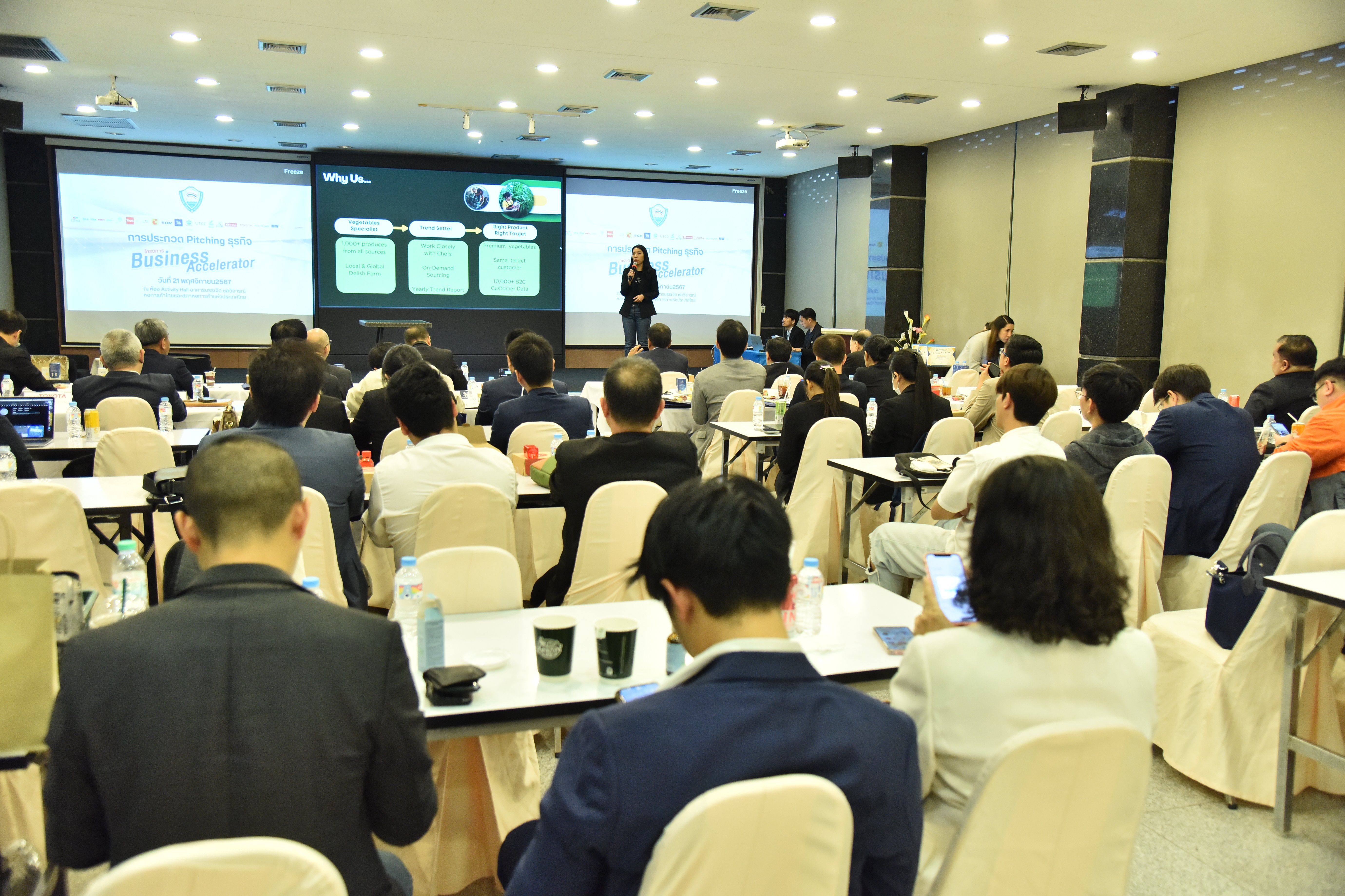 Attendees listen to a presenter speak in a large conference room with dual projection screens.